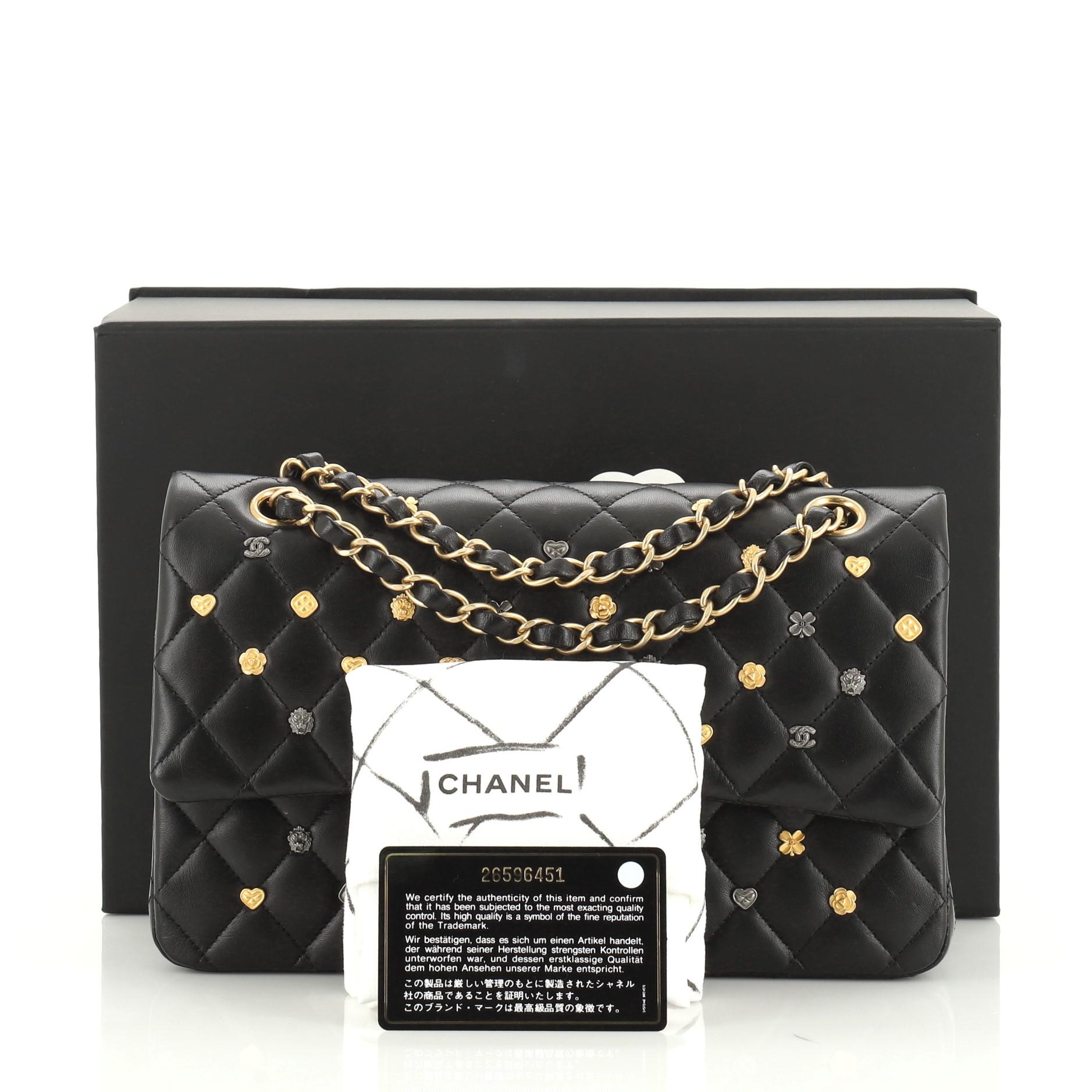 This Chanel 18K Charms Classic Double Flap Bag Quilted Lambskin Medium, crafted in black quilted lambskin leather, features woven-in leather chain link strap, decorated with various charms like the tiny hearts, Camellia flowers and the classic CC