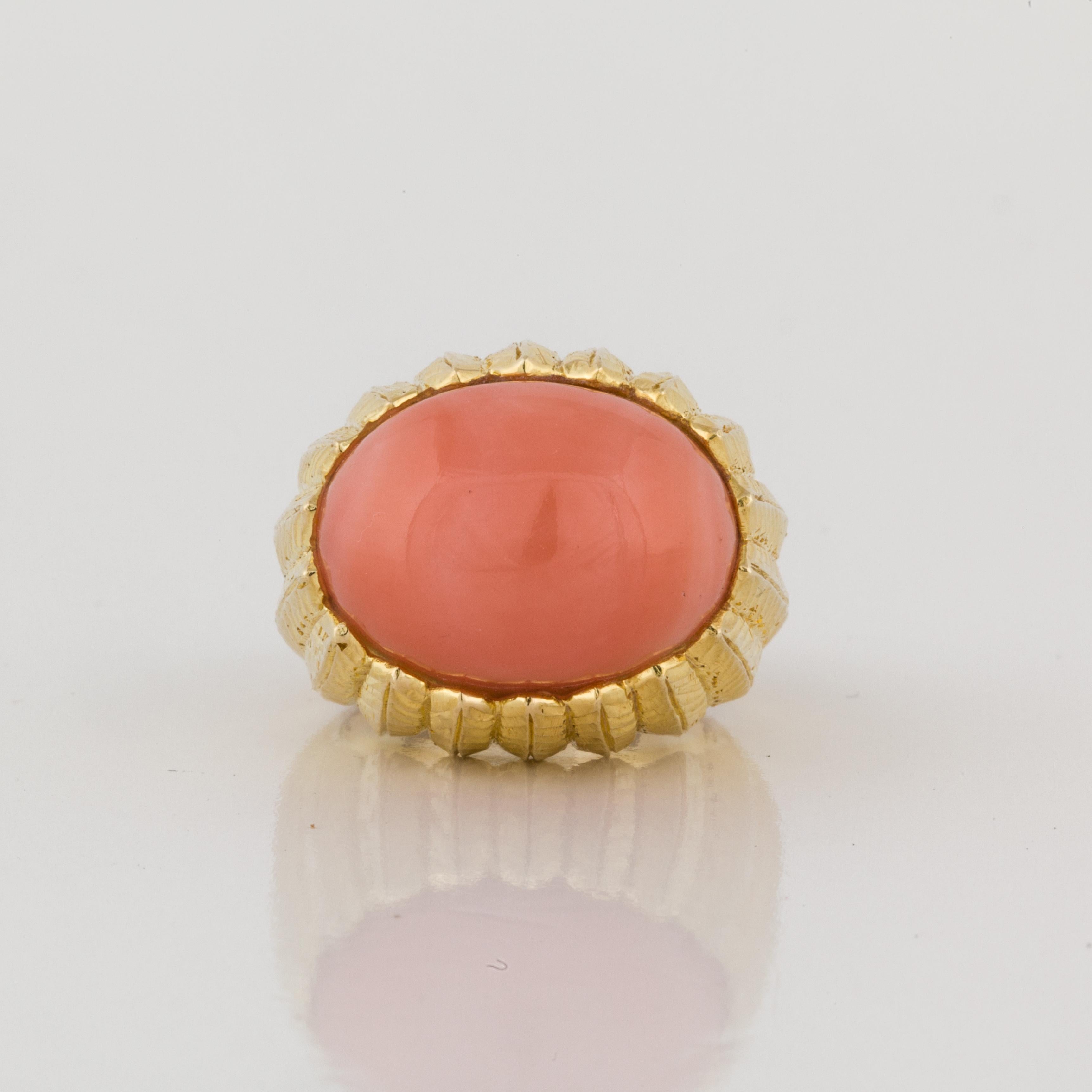 18K hand chased gold ring featuring an oval cabochon coral.  Measures 7/8 inches long by 3/4 inches wide and stands 5/8 inches off the finger.
