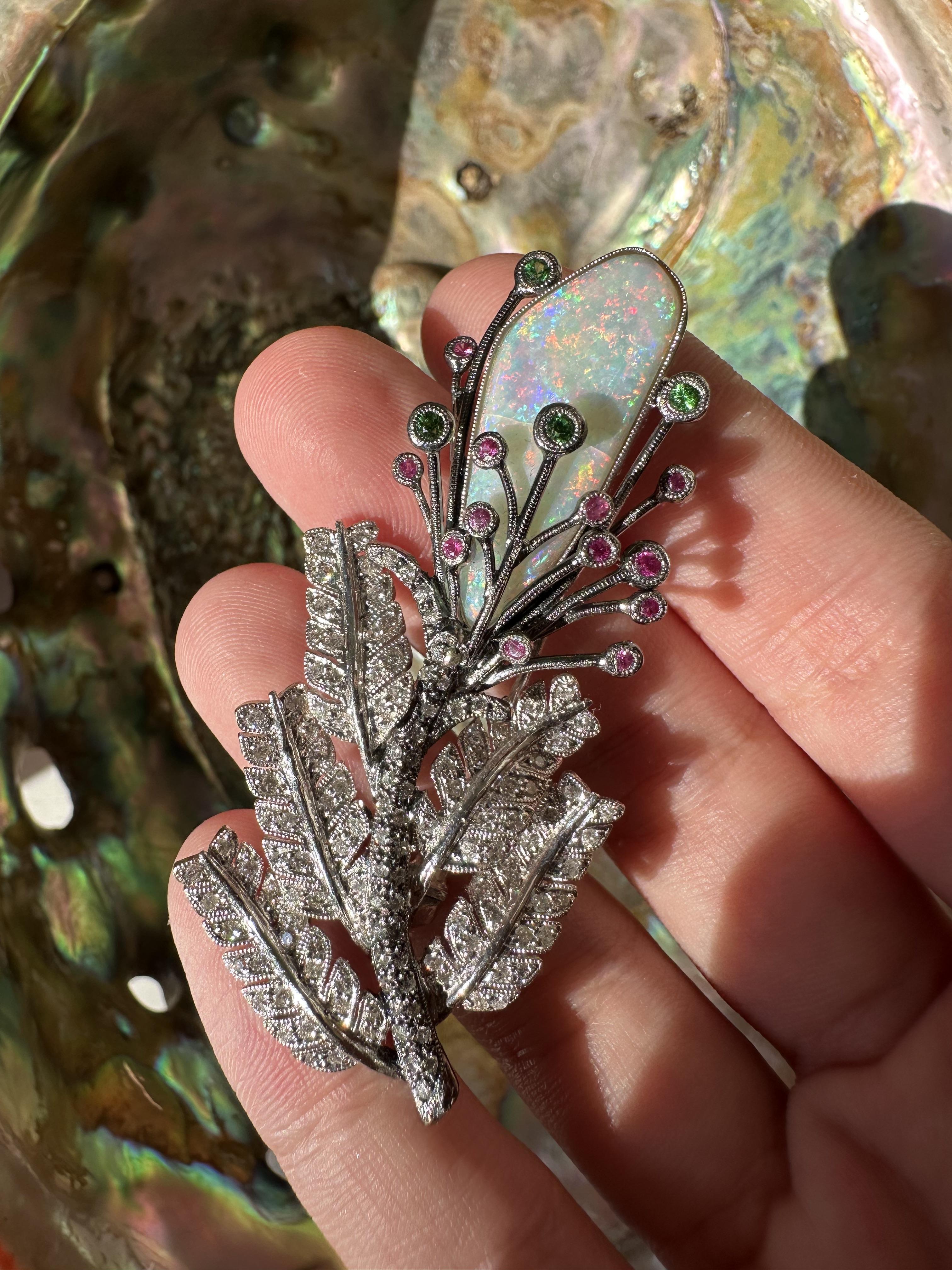 Eine auffällige, von der Botanik inspirierte Brosche mit einem leuchtenden Opal von 7,11 Karat, der von rosa und grünen Saphiren umrahmt wird und auf einem mit Diamanten besetzten Blattmuster sitzt. Gefertigt aus 18 Karat Weißgold mit durchgehender