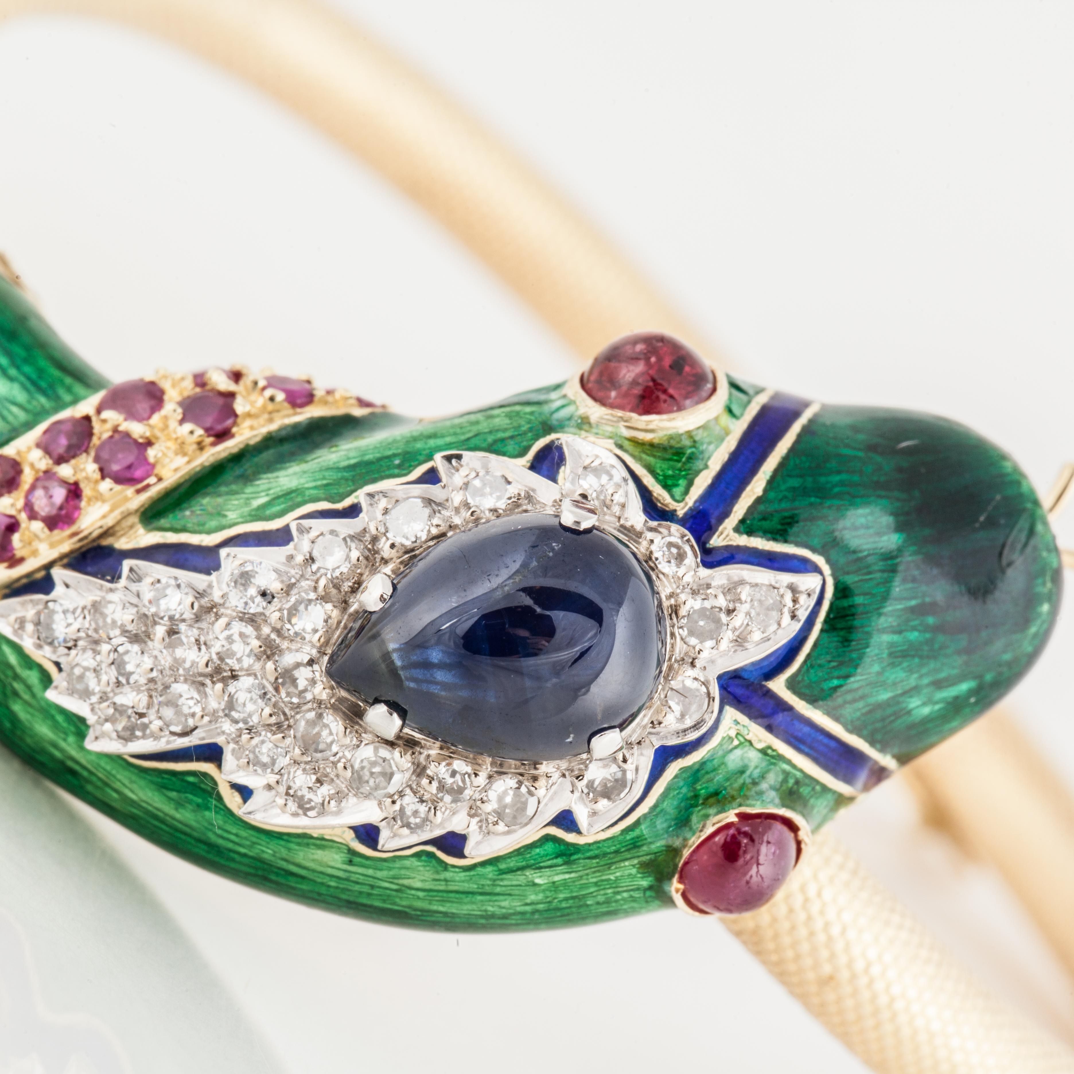 18K yellow gold hinged bangle with a jeweled and enameled snake's head.  The head of the snake is green and blue enamel with a pear-shaped cabochon sapphire.  There are 19 rubies and 45 round diamonds, with a total diamond weight of 0.75 carats. 