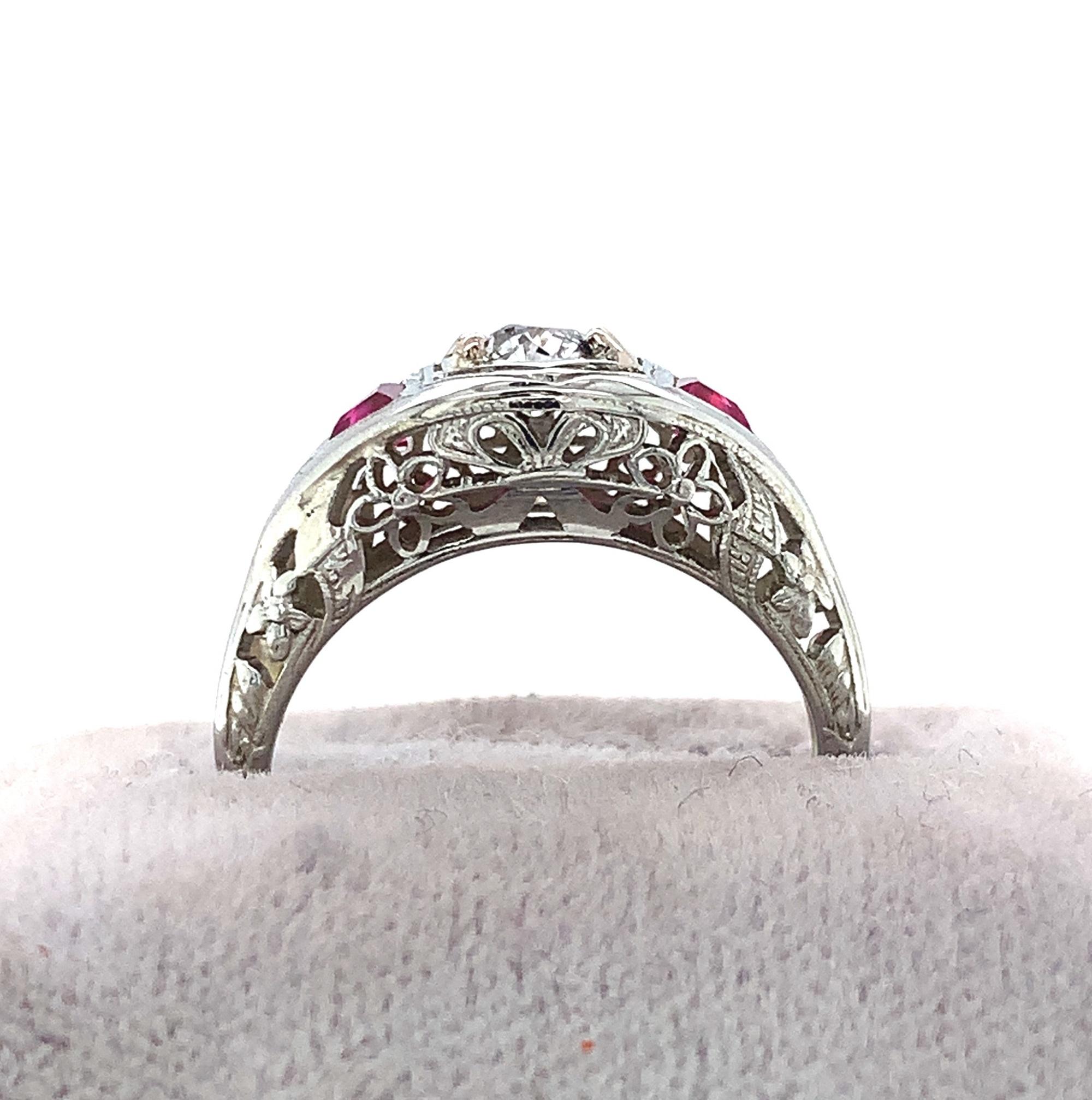 18K white gold filigree Art Deco diamond ring. The European cut diamond weighs .30cts and is accented by a pair of specialty triangle cut red synthetic rubies. The diamond measures about 4.25mm with H-I clarity and SI1 clarity. There are 4 new
