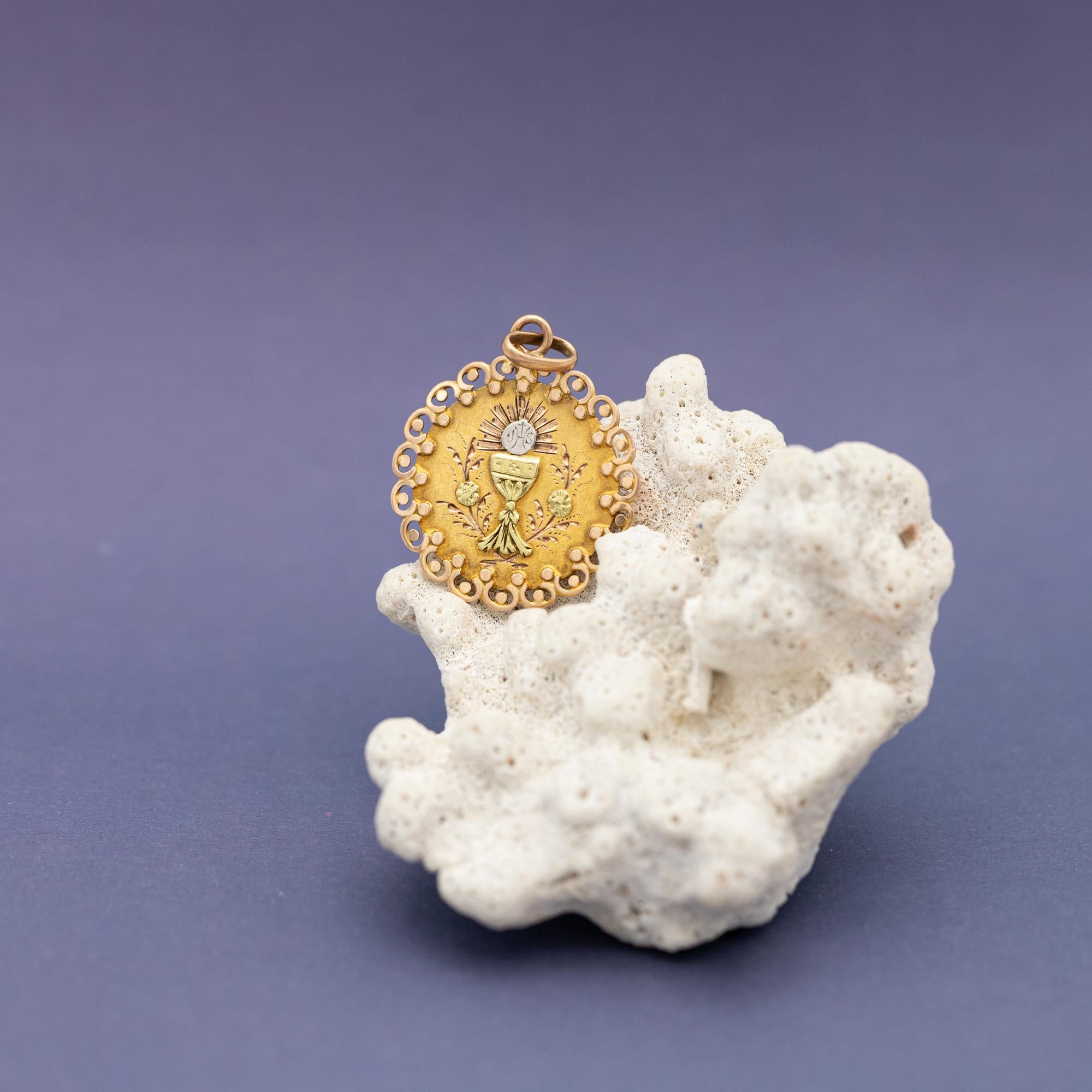 We are delighted to introduce this lovely 18 ct pinkish yellow gold patina medal featuring a chalice, which is a cup often use for drinking during a religious ceremony. A host marked with the letters JHS and a cross is sparkling above it. This