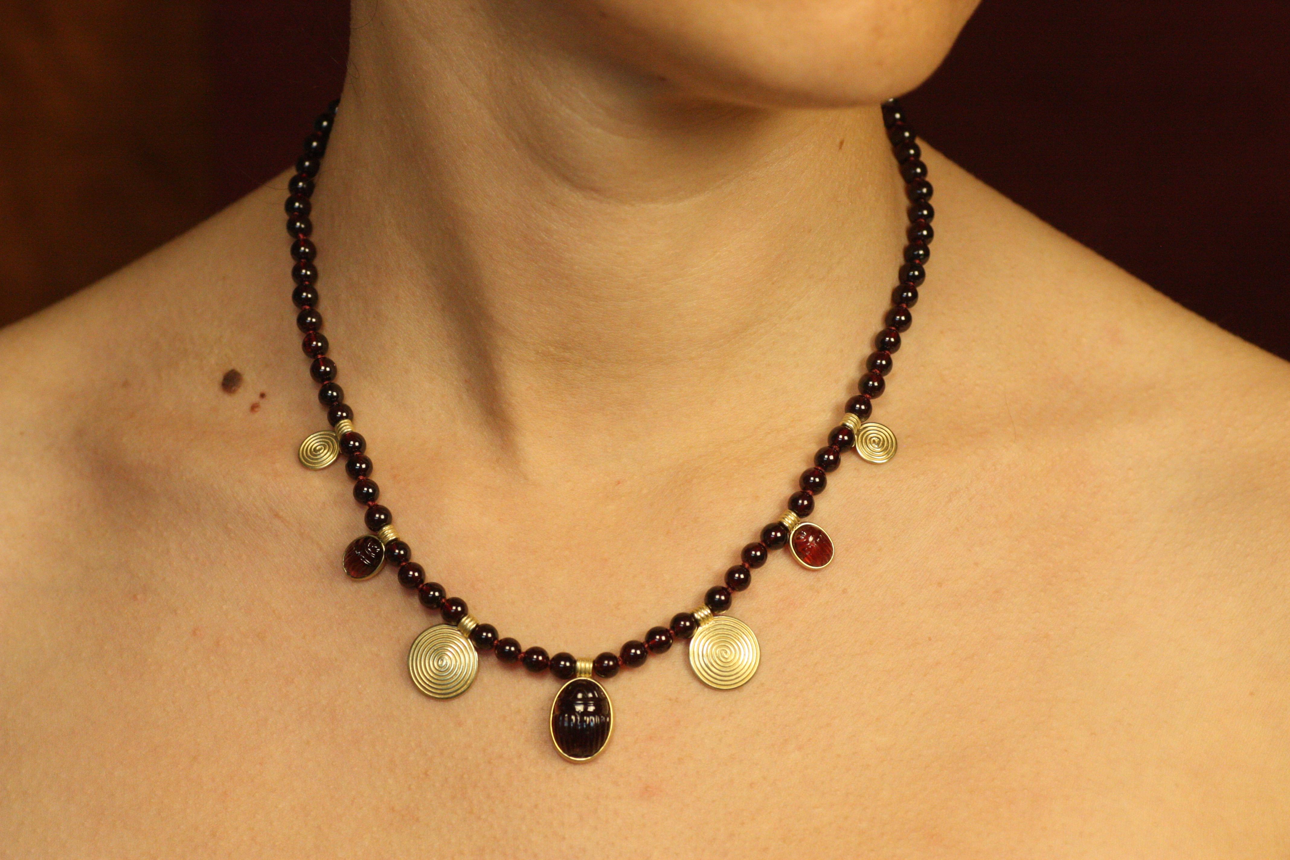 Evoking the mysticism of ancient Egypt, the Scarab Sun Disc Necklace is a luxurious homage to the Egyptian Revival style. This 16-inch masterpiece features rich garnet beads interspersed with luminous 18K yellow gold spiral sun discs. Three