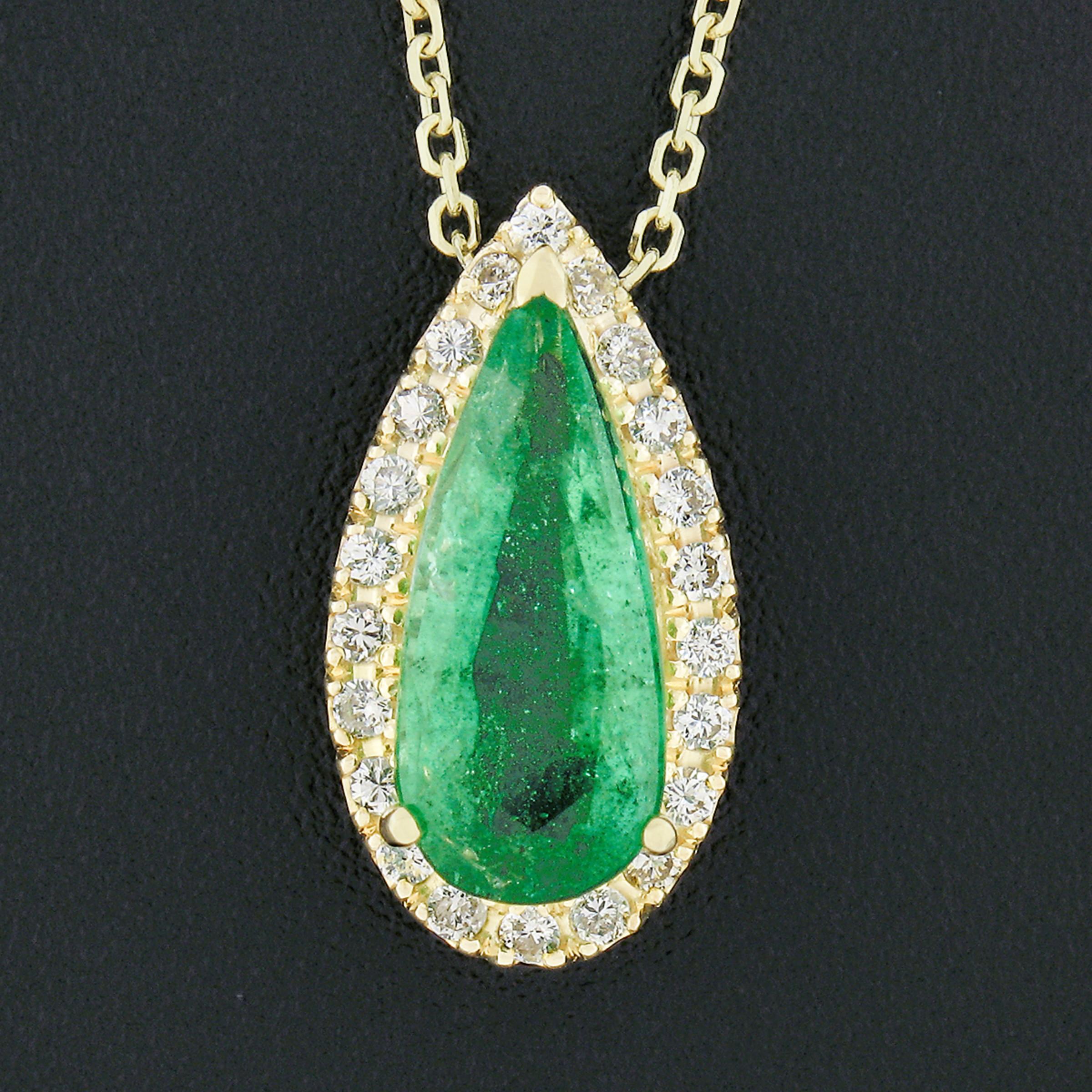 This gorgeous pendant necklace is crafted in solid 18k yellow gold and features an elongated tear drop design set with a fine emerald solitaire and diamond halo. The center carries the neatly set elongated pear cut emerald that shows an attractive