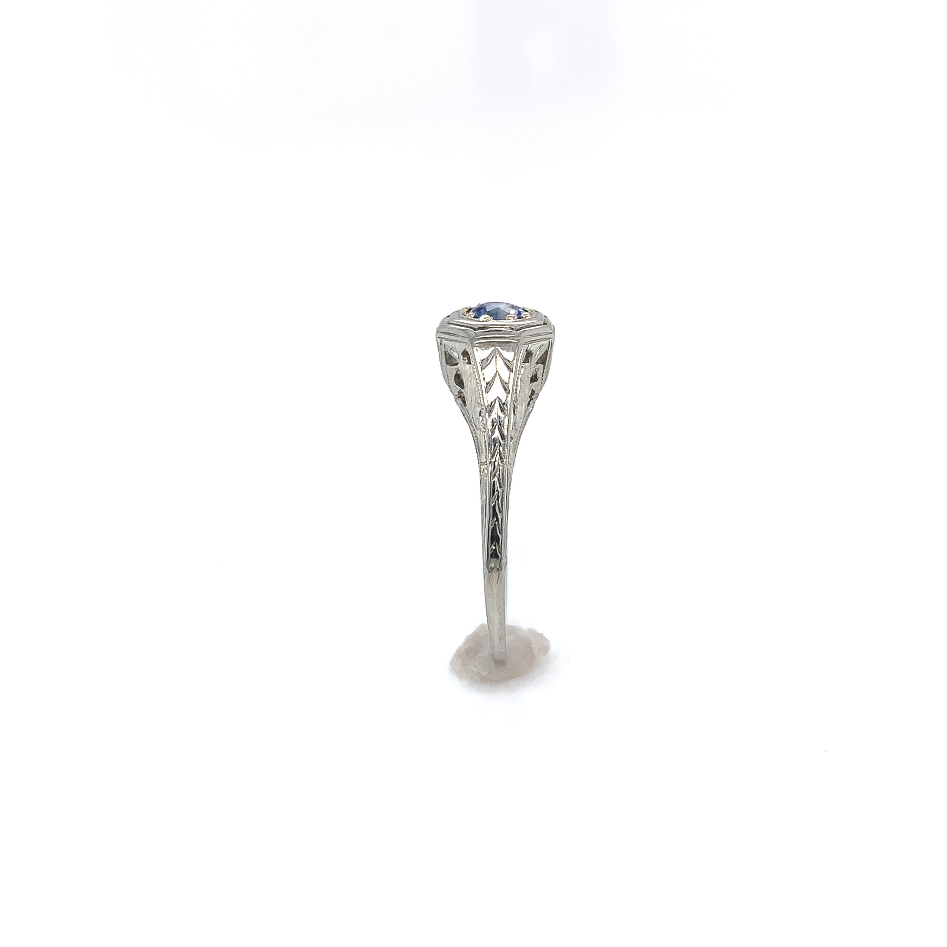 Art Deco 18K white gold filigree ring featuring a round genuine blue sapphire weighing .25cts. The sapphire has medium cornflower blue color and measures about 3.2mm.  There is hand engraved detail and also a little wear where rings were worn beside