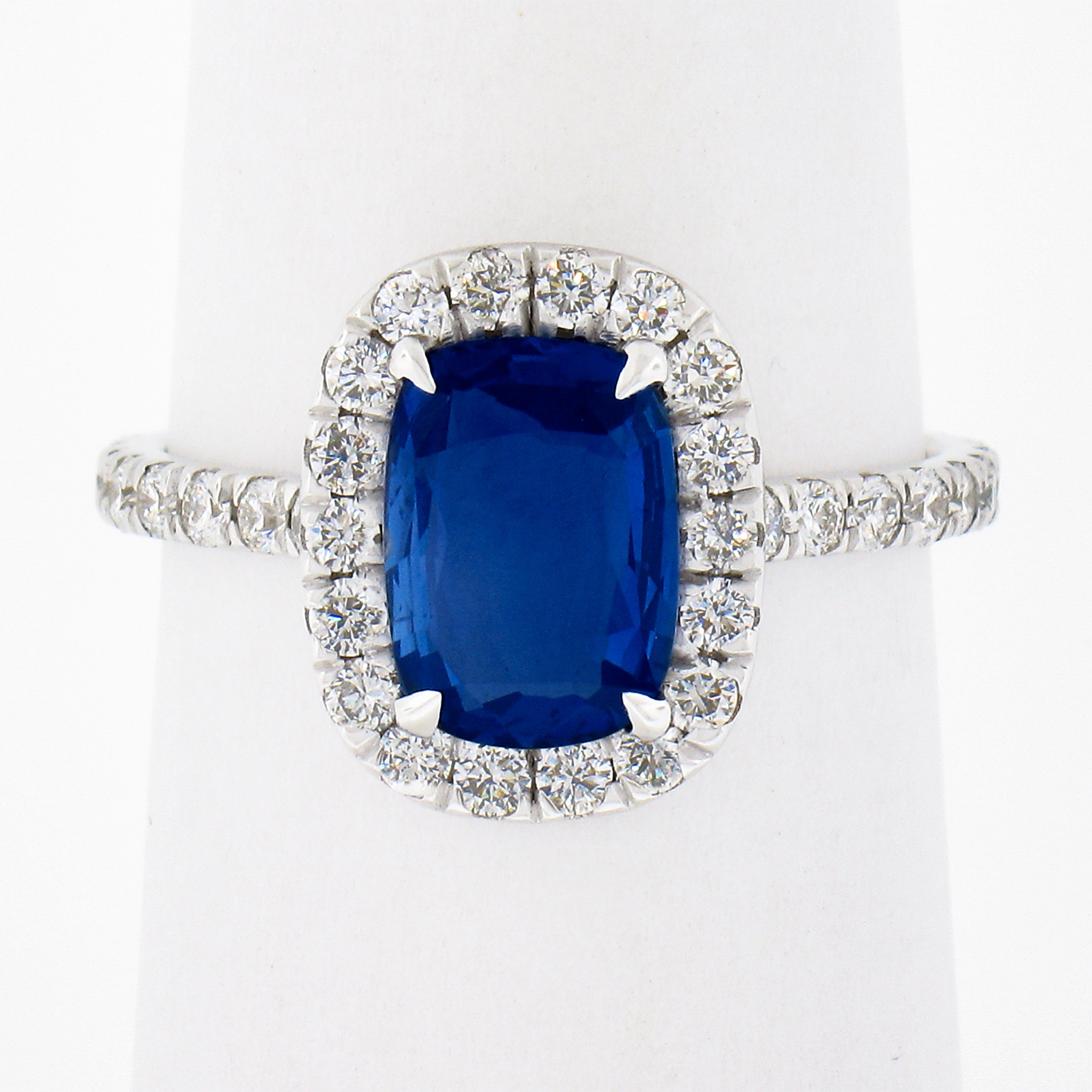 This chic and well made sapphire and diamond engagement ring is newly crafted in solid 18k white gold. It features a cushion, clear and rich blue sapphire that is elegantly claw-prong set at the center of a diamond halo design. The fine quality