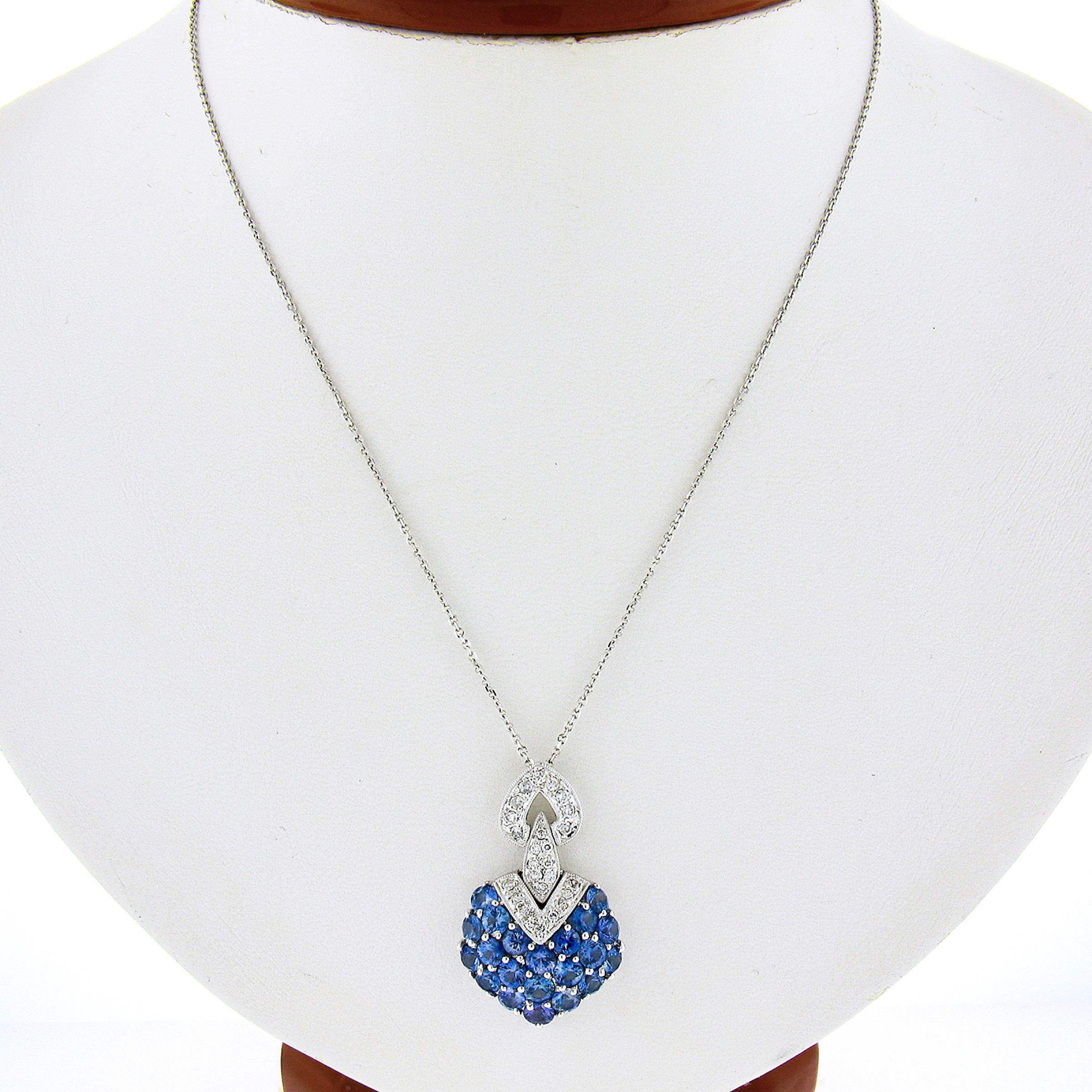 This stunning pendant is crafted in solid 18k white gold and is completely drenched with gorgeous sapphires and diamonds throughout throughout its slightly domed design. The cluster of round brilliant cut sapphires weigh approximately 4 carats in