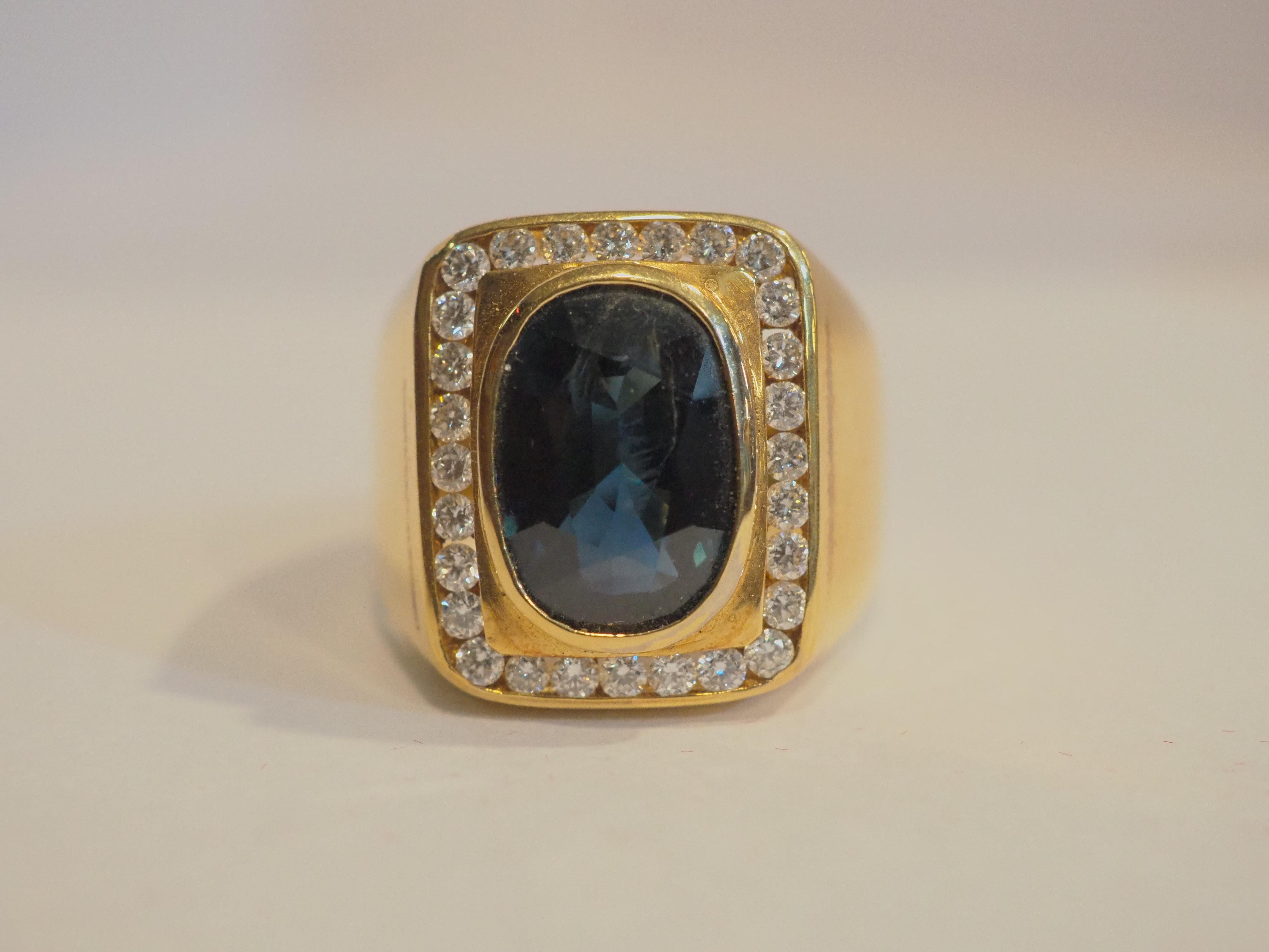  This fantastic cocktail piece is a beautiful 18K yellow gold fine signet ring for man. It features a decent size oval deep blue sapphire as the main gemstone. There is fire and brilliance in the sapphire which is incredible. There are multiple