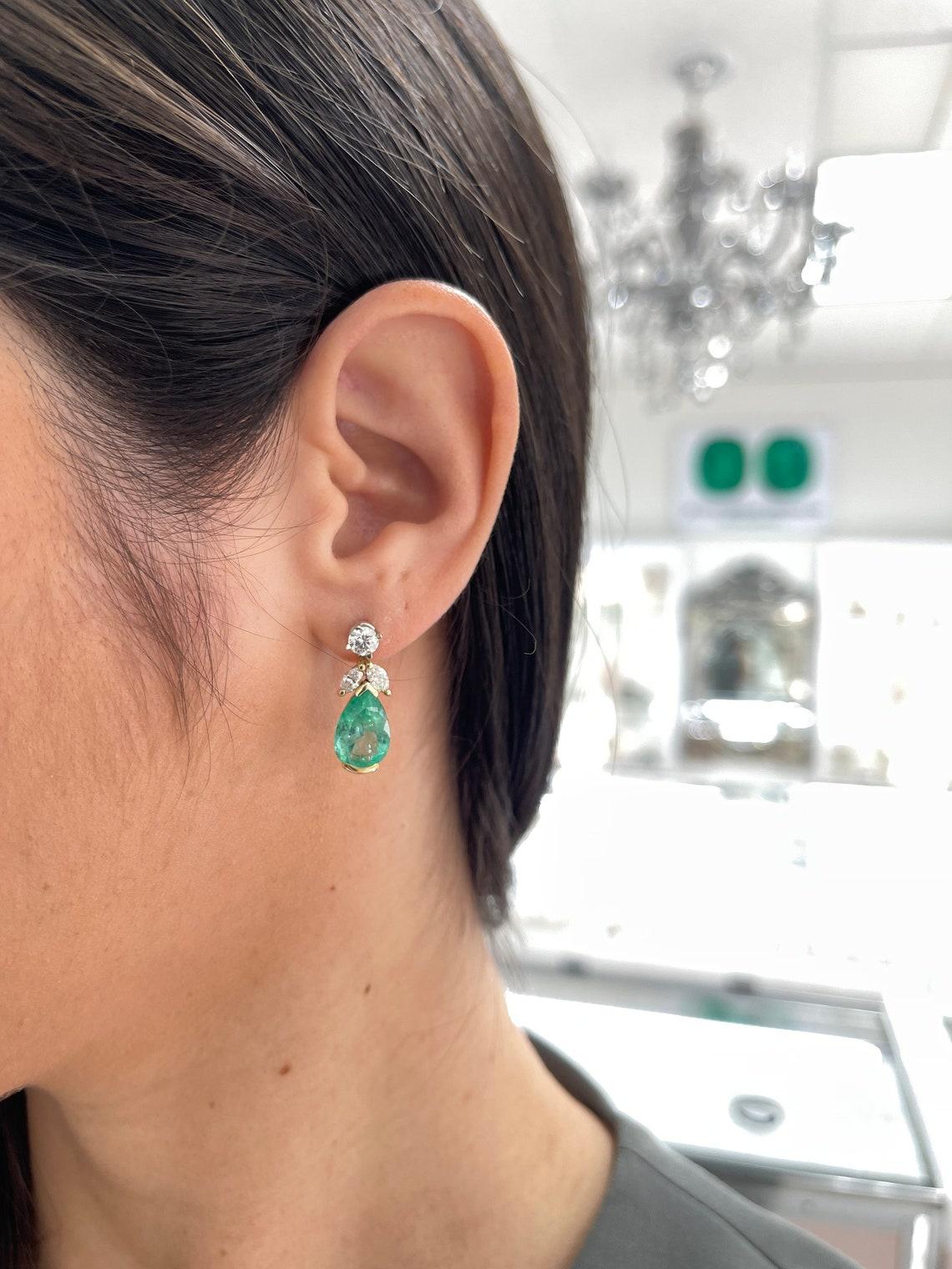 Eleva tu elegancia con nuestros impresionantes pendientes chaqueta con acento de esmeralda y diamantes. Dos exquisitas esmeraldas colombianas talla pera, de color verde medio y claridad semitransparente, están delicadamente engastadas en forma de