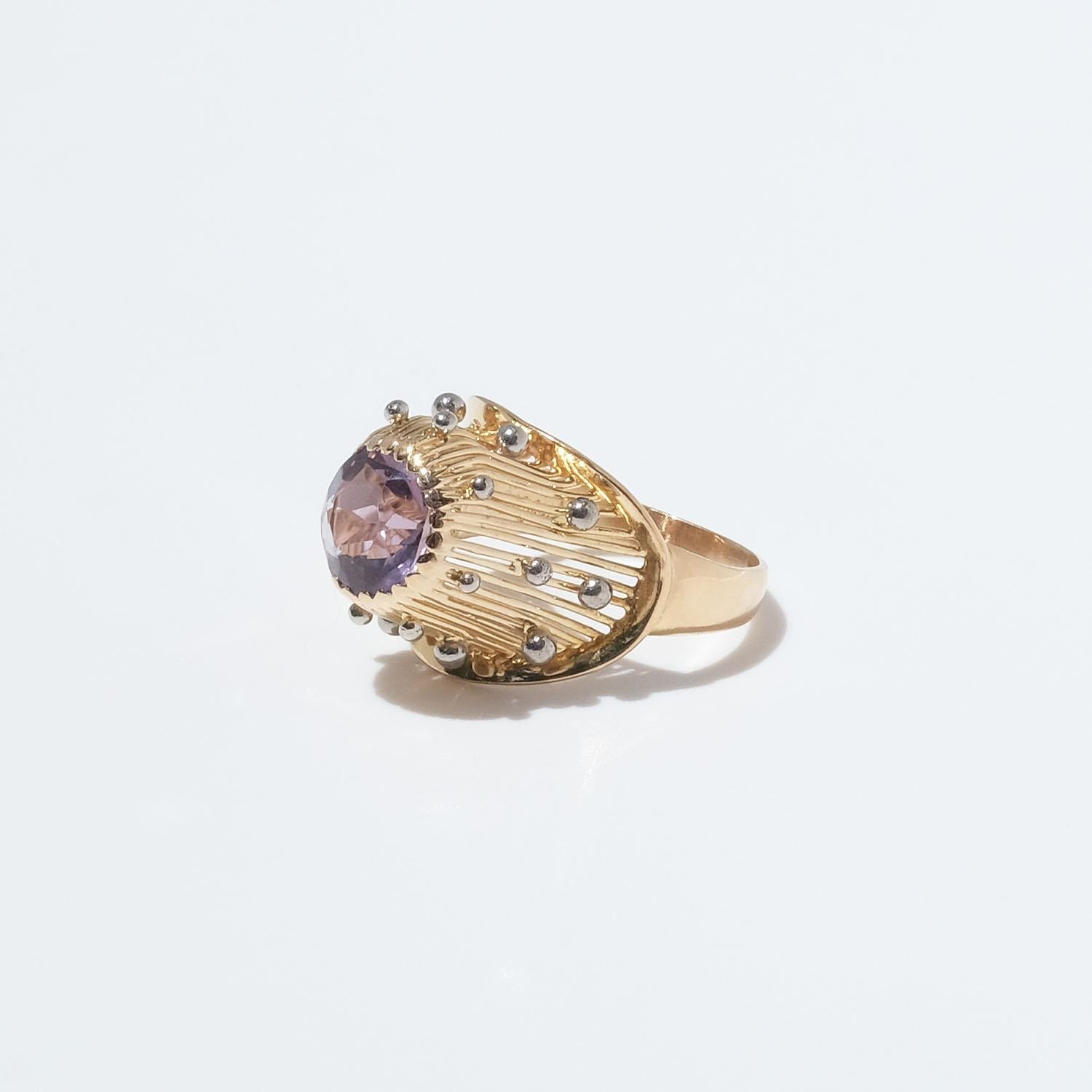 This 18 karat gold ring has a ribbed gallery shaped as a golden cone. The ring is adorned with a light purple amethyst and small silver globes. The ring looks like an intriguing organic creation.

The ring's joyful character and design makes it