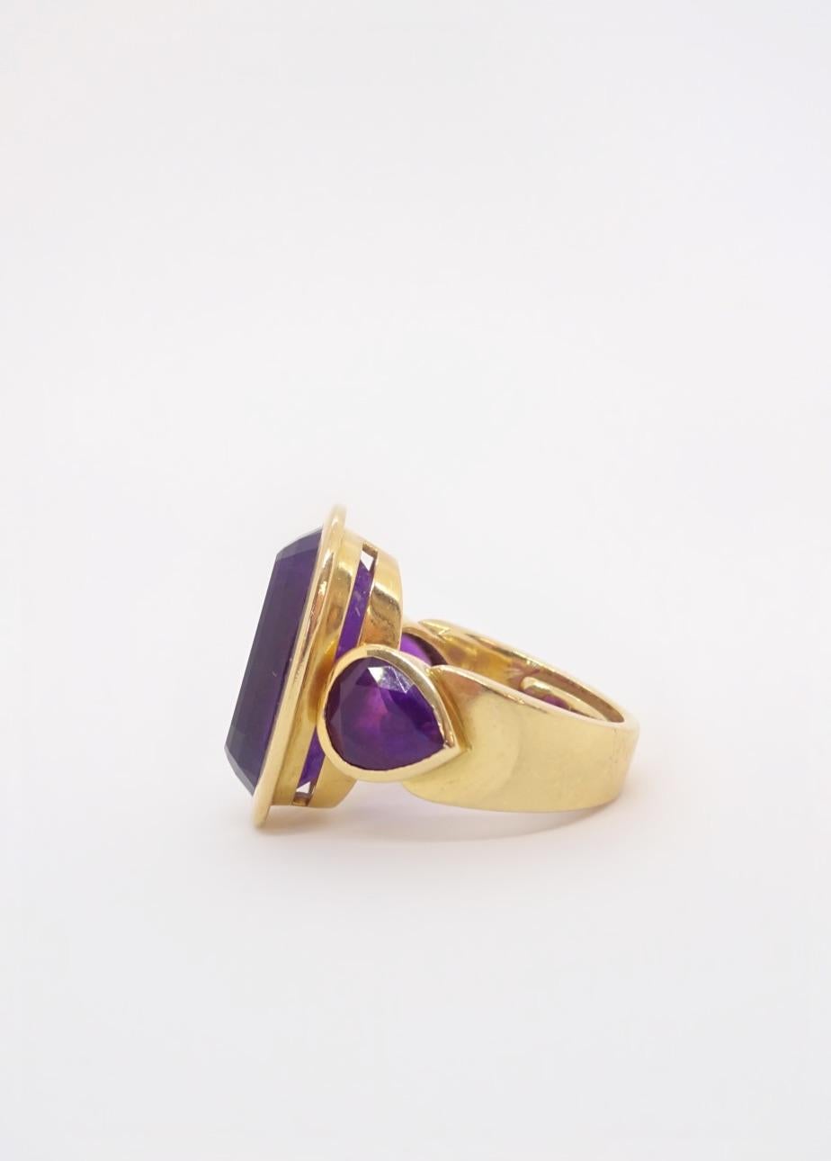 Mod cocktail ring in 18K yellow gold features a gorgeous step-cut amethyst with a royal purple color, flanked by two matched pear shaped amethysts all bezel set for a bold, chunky look.  Size 6