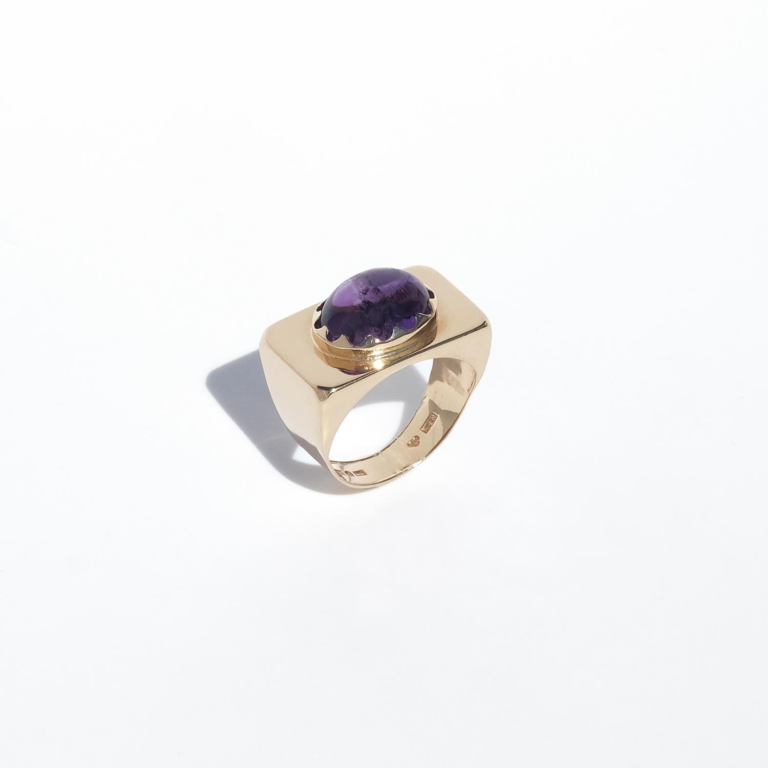 This striking ring is crafted in 18-karat gold and showcases a deep purple amethyst as its centerpiece. The gemstone is smooth-polished in a classic cabochon cut, creating a rich, domed surface that reflects light softly and naturally.

The amethyst