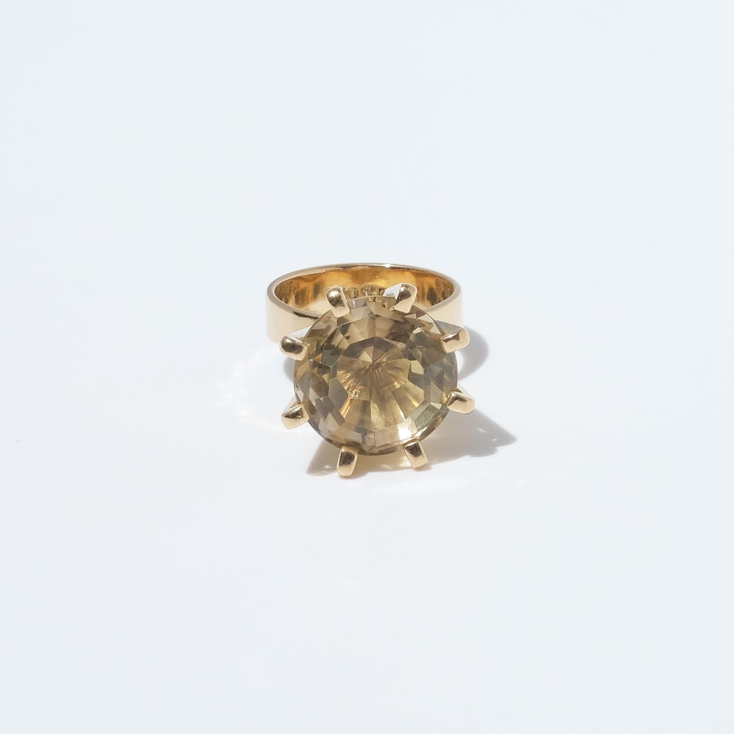 This 18 karat gold ring is adorned with a faceted cut citrine. The head of the stone is distinct and the colour of the stone has a light yellow tone. The prongs are prominent and the shank of the ring changes shape in a subtle and elegant way.

The