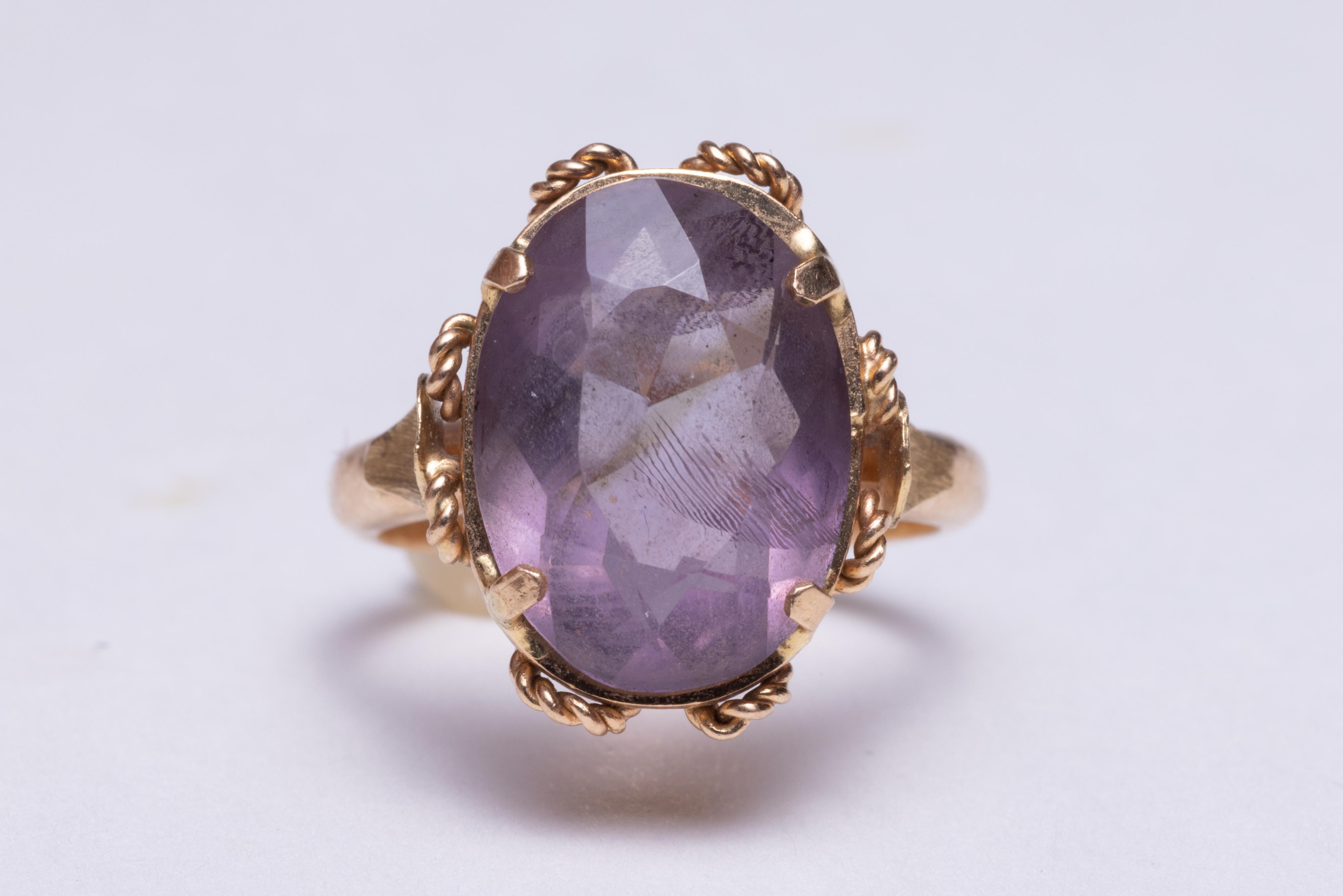 An elegant 18K gold ring with textured wire work as the basket of the stone.  It features a 7 carat, faceted oval amethyst stone.    Ring size is 6.25
