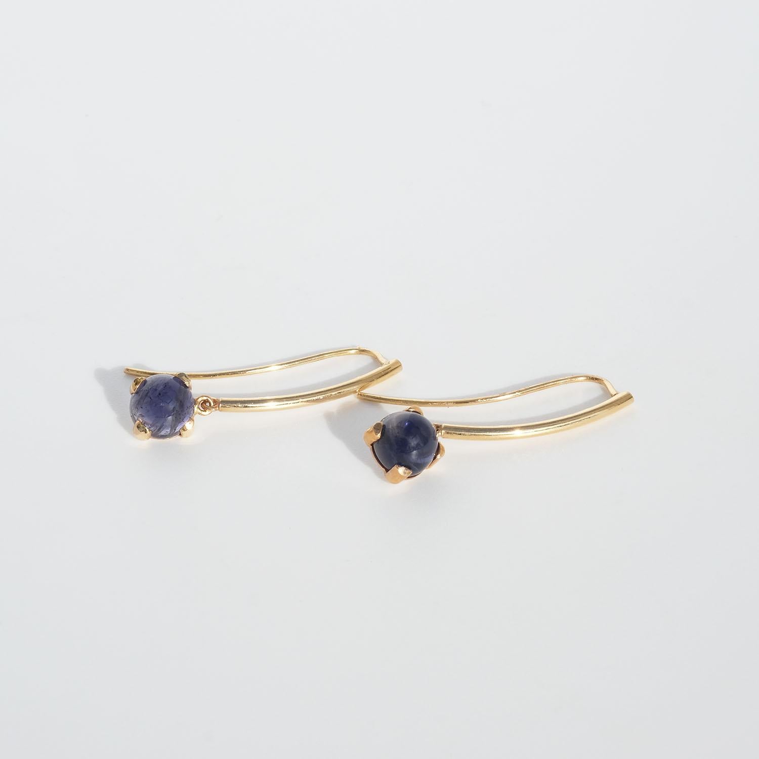 These 18 karat drop earrings are adorned with cabochon cut iolite stones. Each iolite stone has a beautiful violet colour which plays perfectly with the golden colour of the bars. To keep the earrings in place hooks are used. 

The earrings have a