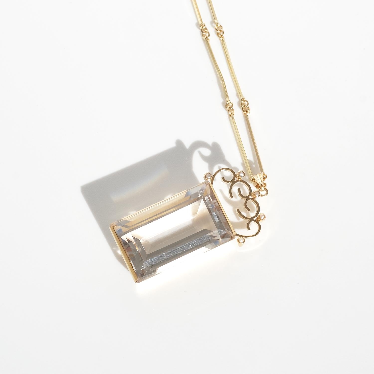 This vintage necklace in 18 karat gold features a rectangular rock crystal pendant with an ornate gold top adorned with delicate small pearls, resembling a monogram design. The pendant hangs from a refined bar-and-ring chain, with elongated gold