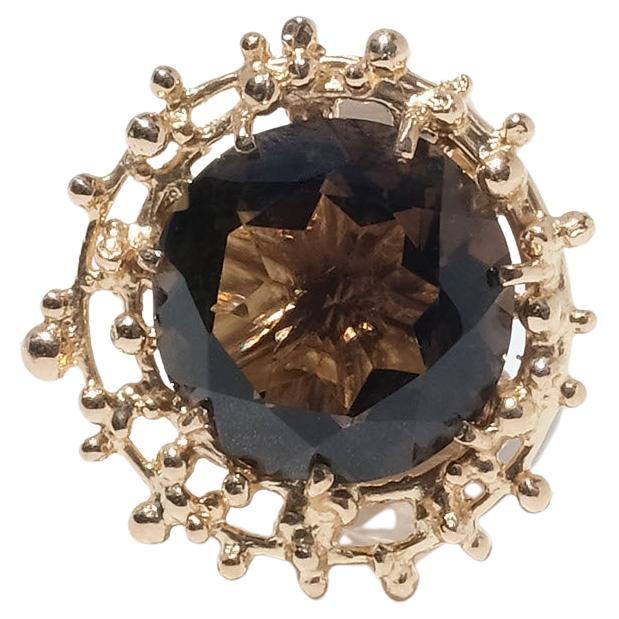 This 18 karat gold ring is adorned with a brilliant cut smoky quartz. The head of the stone is distinct as is the wide shank. The ring has an amazing round setting, which makes the ring resemble a sunflower.

The ring is both a happy piece as well