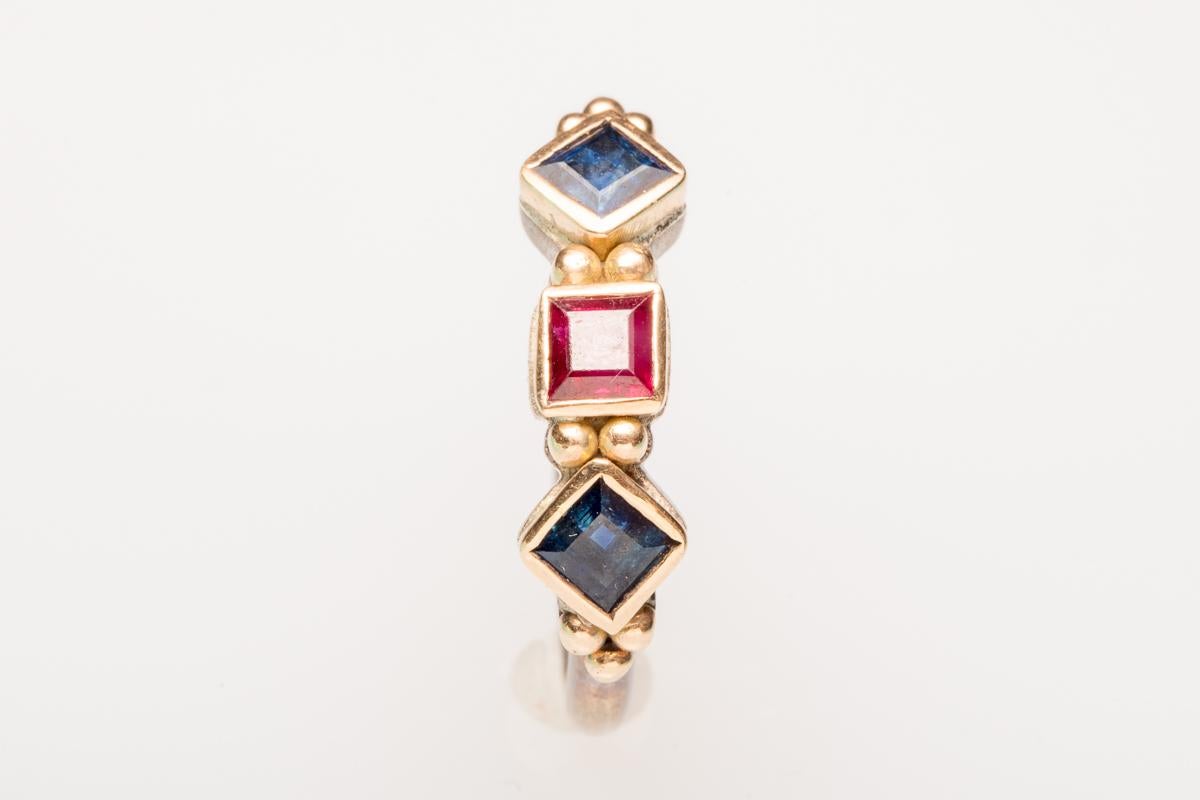 Square-cut ruby flanked by two blue sapphires set in a weighted (not plated) 18K gold and sterling silver band.  Total carat weight of stones is 1.5.  Gold granulation work between and bordering stones.  Ring size is 7.25.