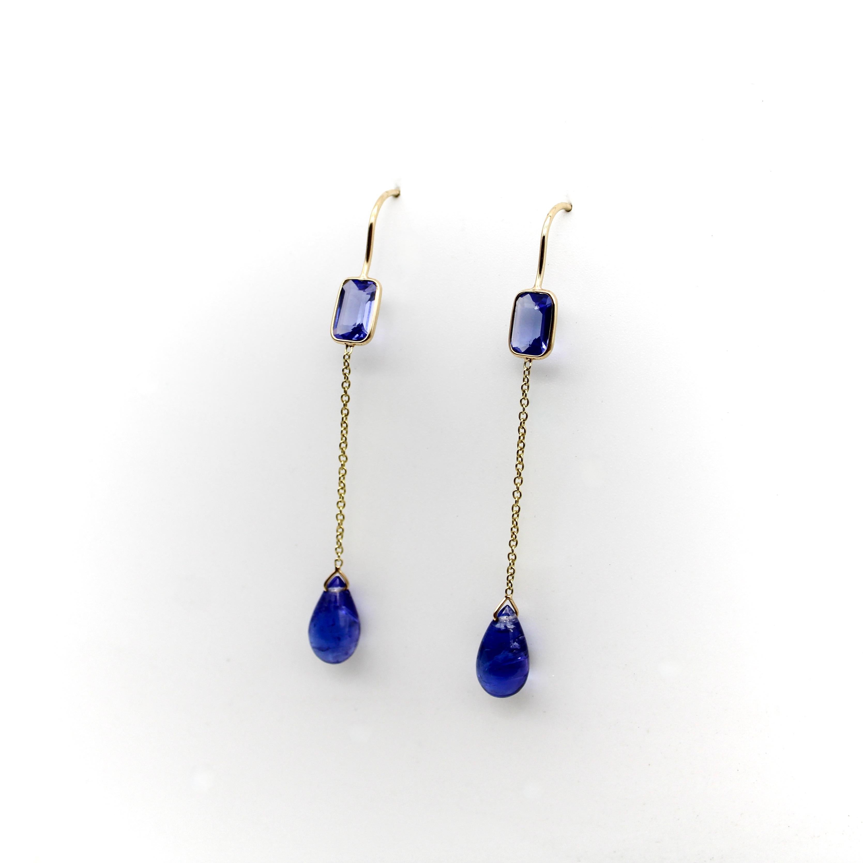 Stunning blue tanzanites are set in 18k gold, with an emerald cut stone at the top and a teardrop shaped stone dangling from a delicate piece of gold chain. The tanzanites are a beautiful blue with purple undertones, rich and saturated, yet with a