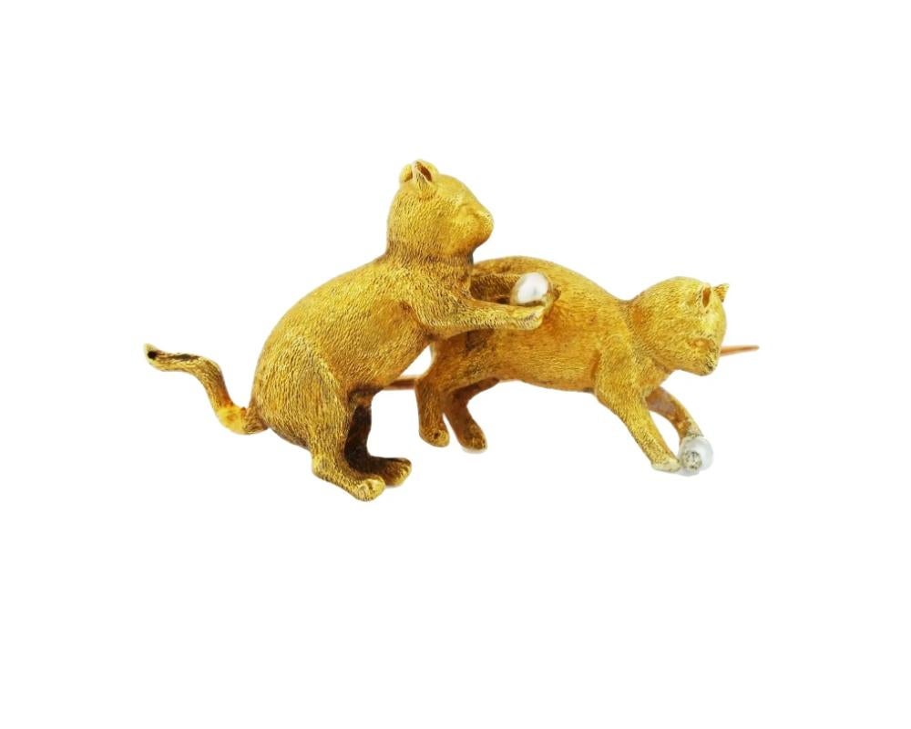 An antique 18K Yellow Gold figural brooch. The brooch is decorated with two figurines representing cats playing with natural pearls. The brooch is adorned with engraved detailed patterns. Marked with two impressed marks. Antique and Vintage Gold