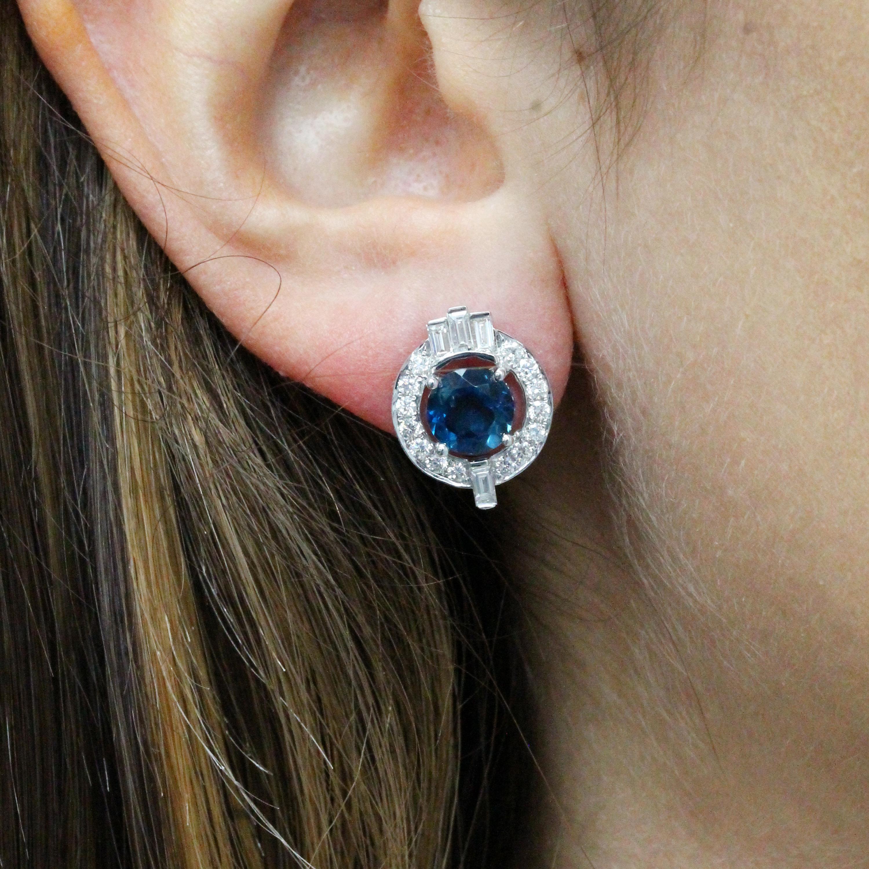 ohrstecker im Art-Deco-Stil aus 18 Karat Weißgold mit rundem, zackenbesetztem Londoner Blautopas, rundem Diamant-Halo und Baguette-Diamant-Akzenten. Über 1 Karat Diamanten lassen diese Ohrringe glänzen. Post- und Pushback-Verschluss. Einzigartiger