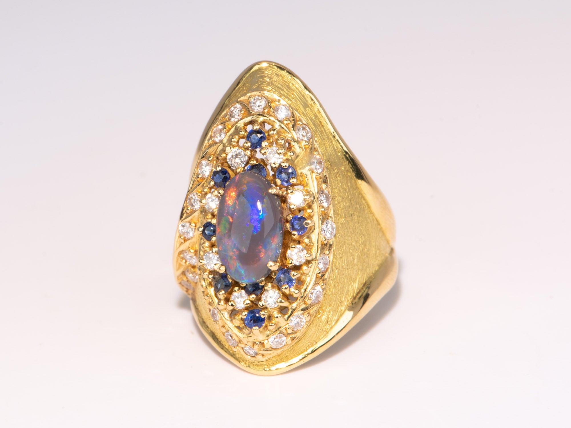  Cette bague en or 18 carats en saphir et diamant d'opale noire australienne est un bijou époustouflant qui fera tourner les têtes ! Sa forme allongée s'harmonise avec la magnifique opale qui brille d'éclats rouges, bleus et orange. Son éclat et sa