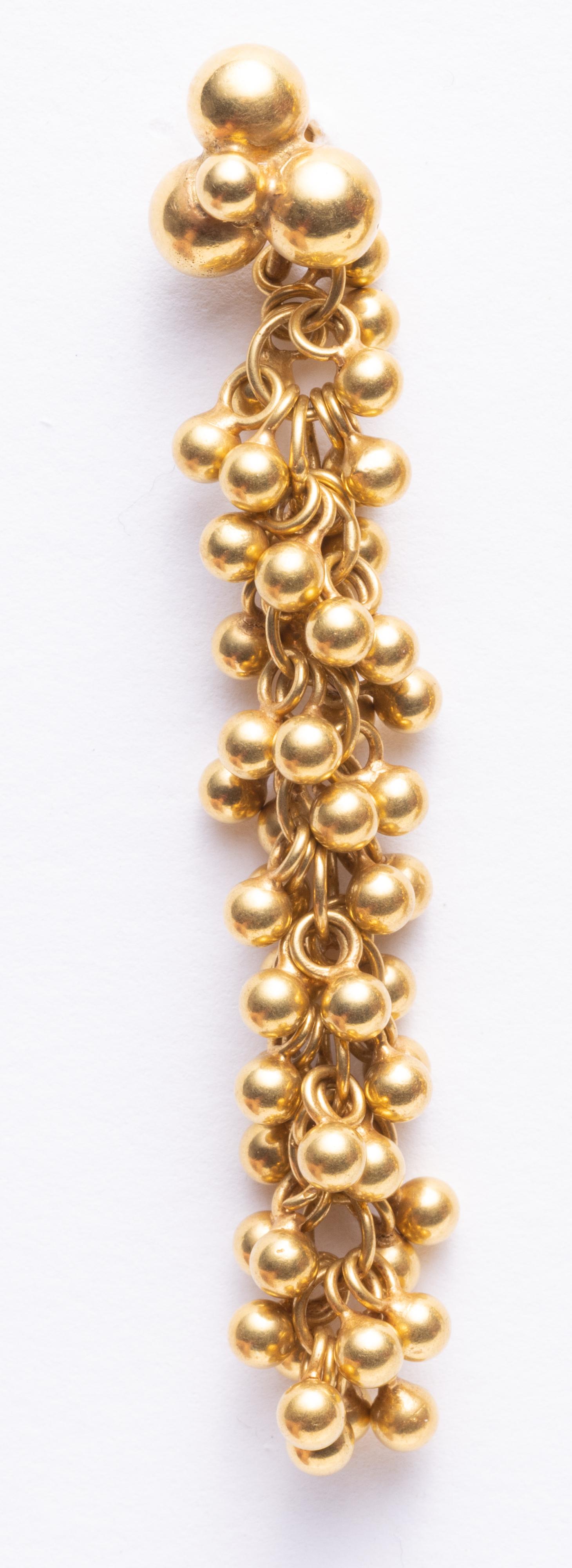 Une paire de boules d'or 18K perlées de façon complexe et tissées sur une longue chaîne, créant une boucle d'oreille longue et texturée avec du mouvement.  Des boules d'or plus grosses forment le tenon au niveau du lobe, pour les oreilles percées.