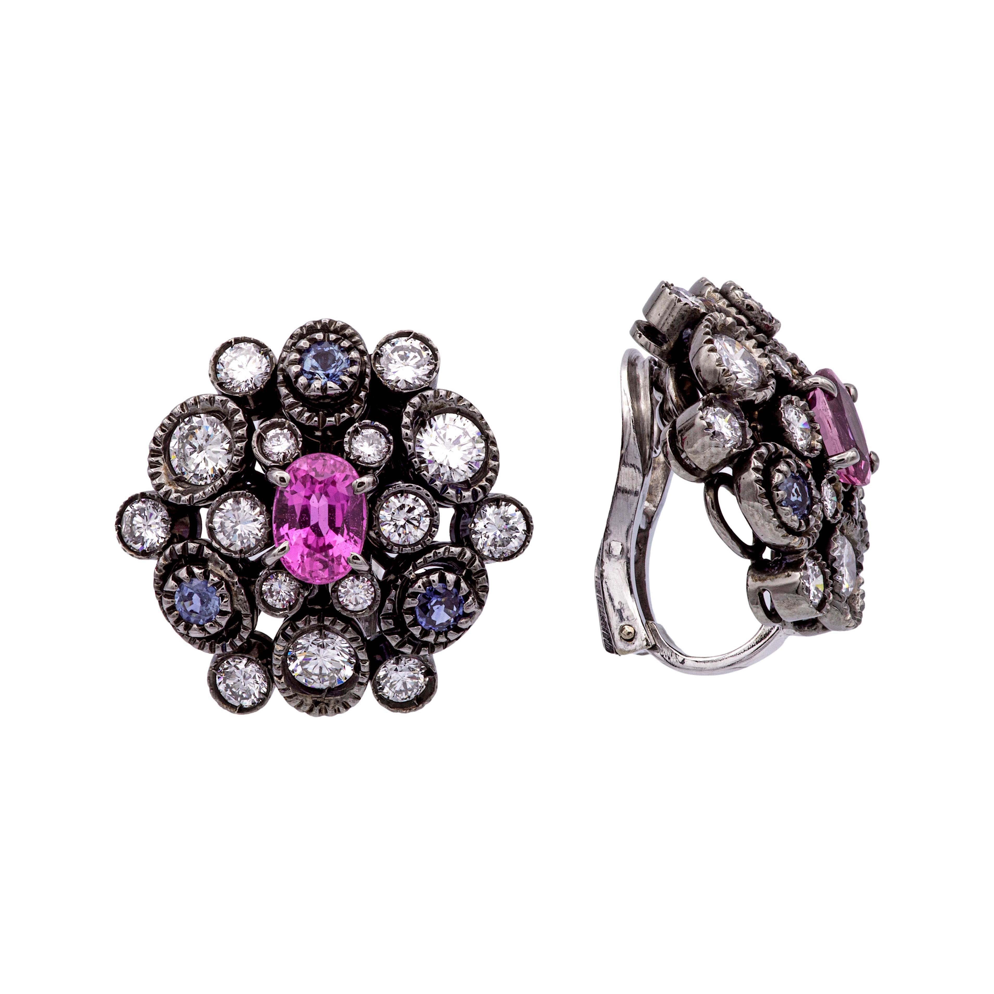 Pair of cluster earrings finely crafted in black rhodium on top of 18 karat white gold featuring an oval pink sapphire center set in claw prongs , each weighing an approximate of 0.75 carats adorned by 6 round blue sapphire intermixing with 30 round
