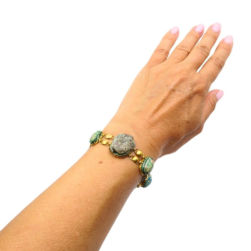 This exquisite bracelet melds ancient symbolism with modern elegance. Crafted in 18k yellow gold, it highlights a stunning sequence of genuine ancient scarabs—likely glazed steatite, a signature material in Egyptian jewelry—each unique in color and