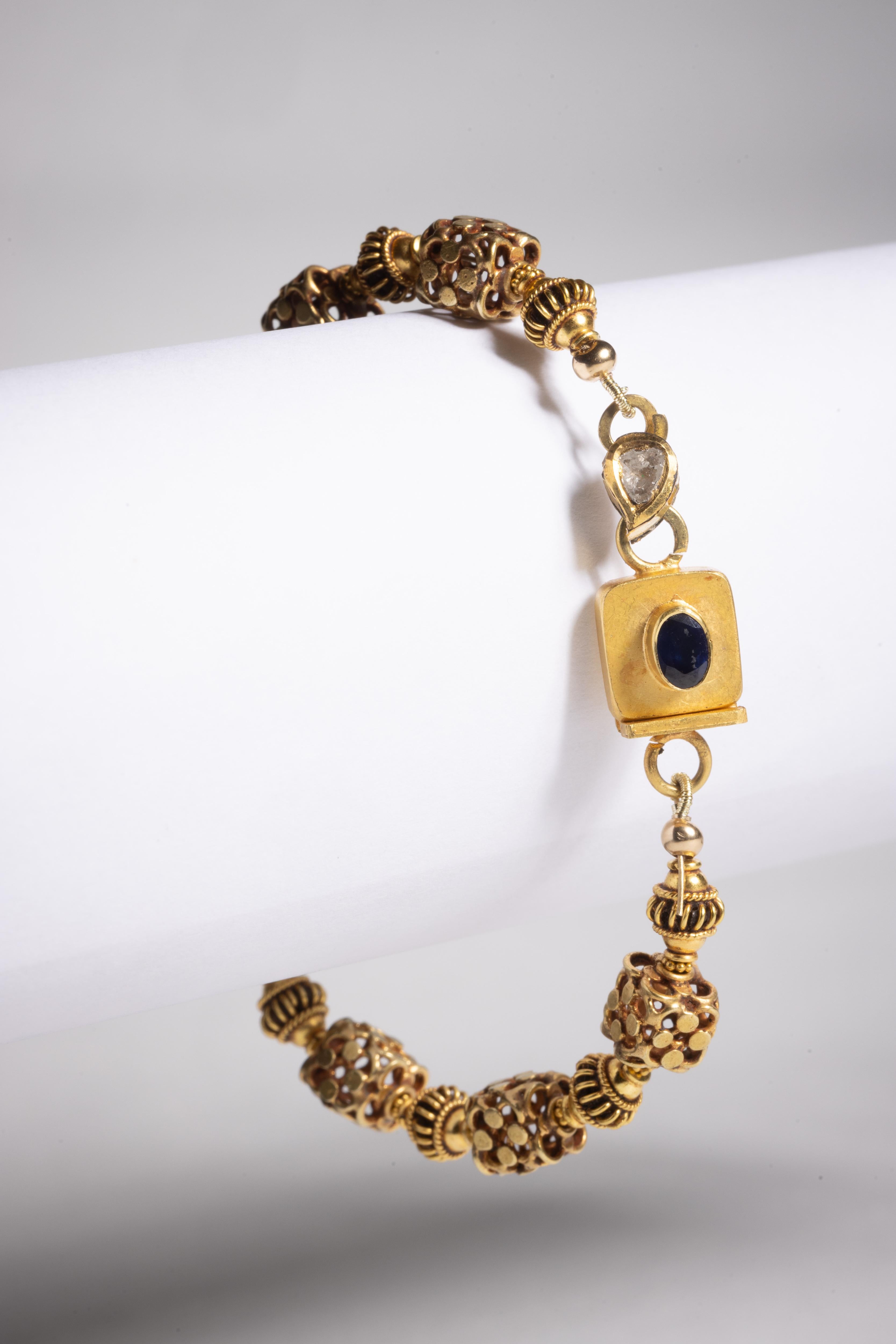 An 18 karat gold beaded bracelet with very unusual hand made beads adding texture and dimension.  The push clasp features a faceted oval blue sapphire and a rosecut diamond on one side with enamel work on the back of the diamond.

The fine jewelry