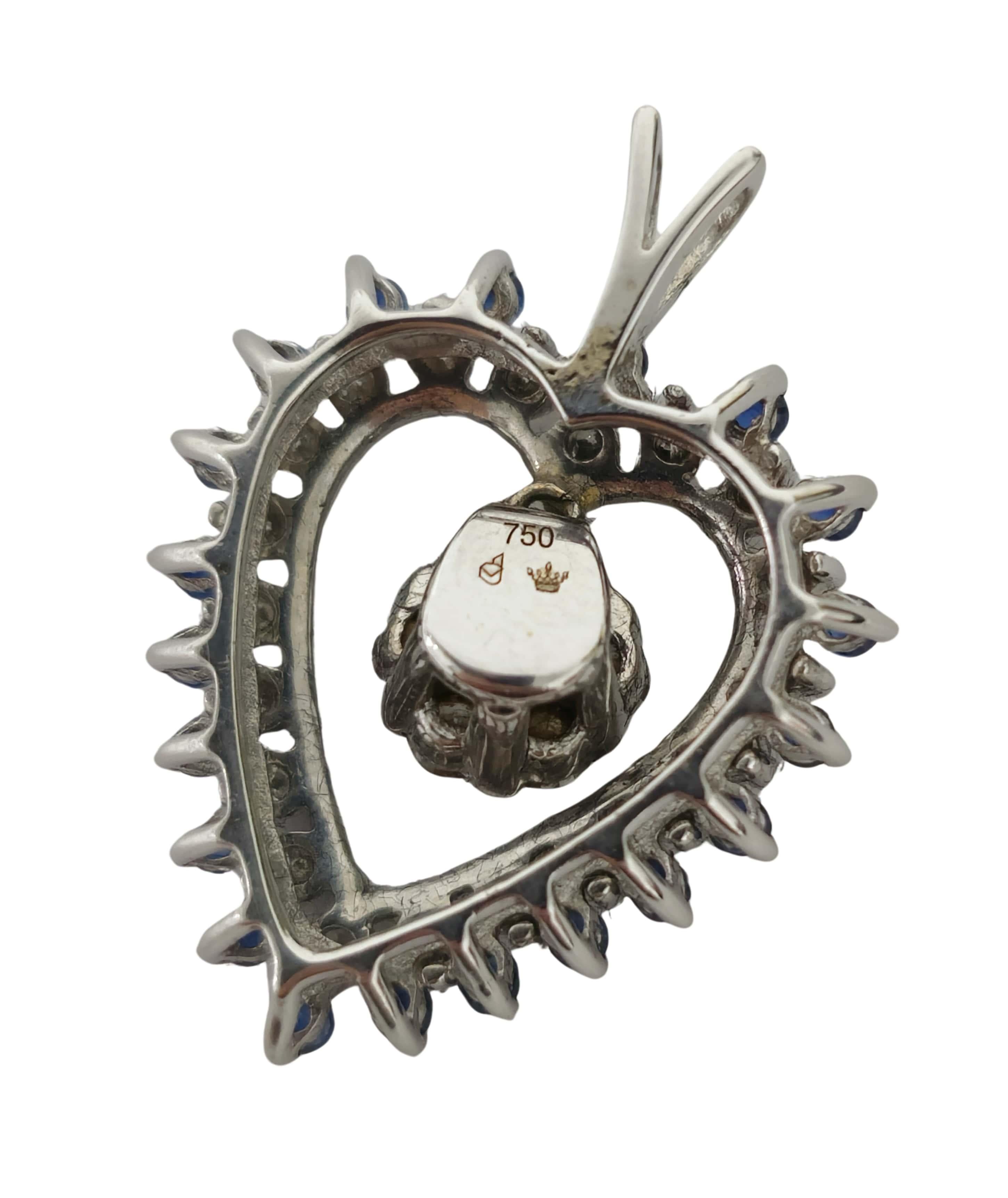 Realizzato in oro bianco 18 carati, questo pendente presenta uno zaffiro blu a forma di cuore ornato da diamanti rotondi di alta qualità con taglio a brillante. I diamanti vantano un colore F e una purezza VS, garantendo una brillantezza e uno