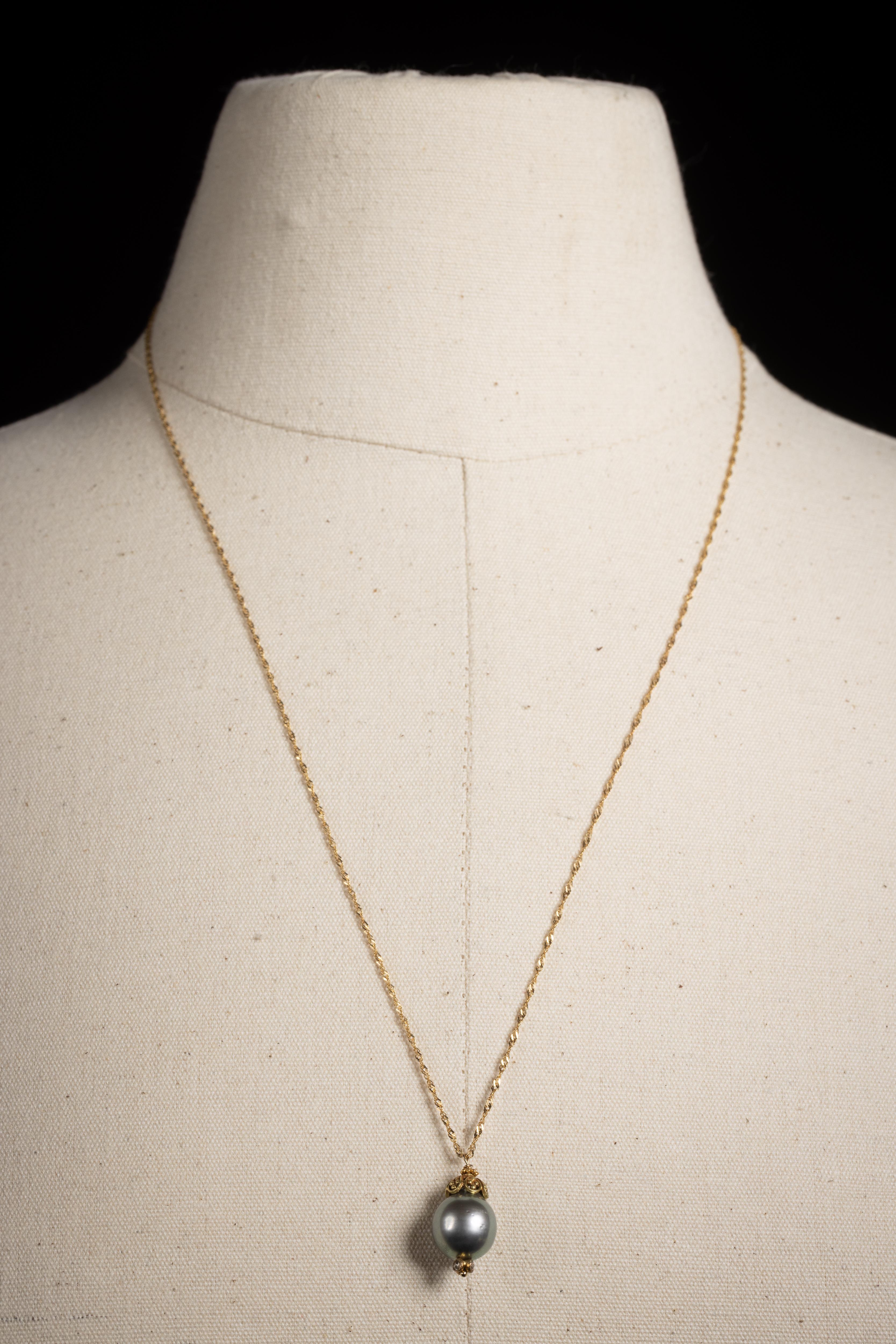 Un elegante pendente di perle di Tahiti da 12 mm con tre diamanti rotondi sfaccettati in oro 18 carati nella parte inferiore e un tappo in oro 18 carati con una raffinata lavorazione a graffio nella parte superiore.  La catena in oro 18 carati è una