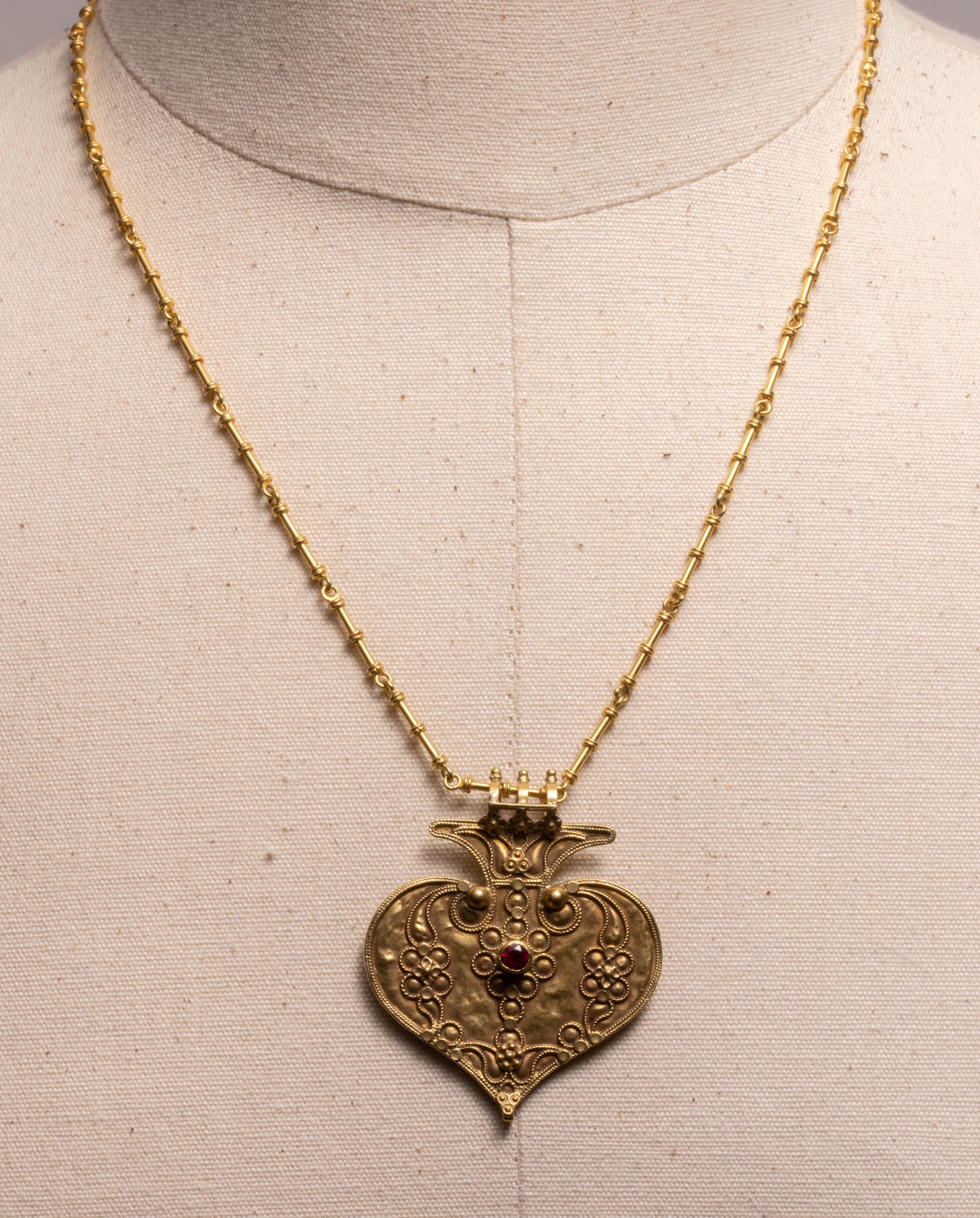 An 18K gold hand-tooled linked chain with an Indian spade-shaped pendant with fine granulation work and hand tooling.  A round pink spinel is set in the middle of the pendant.  The pendant itself measures 2