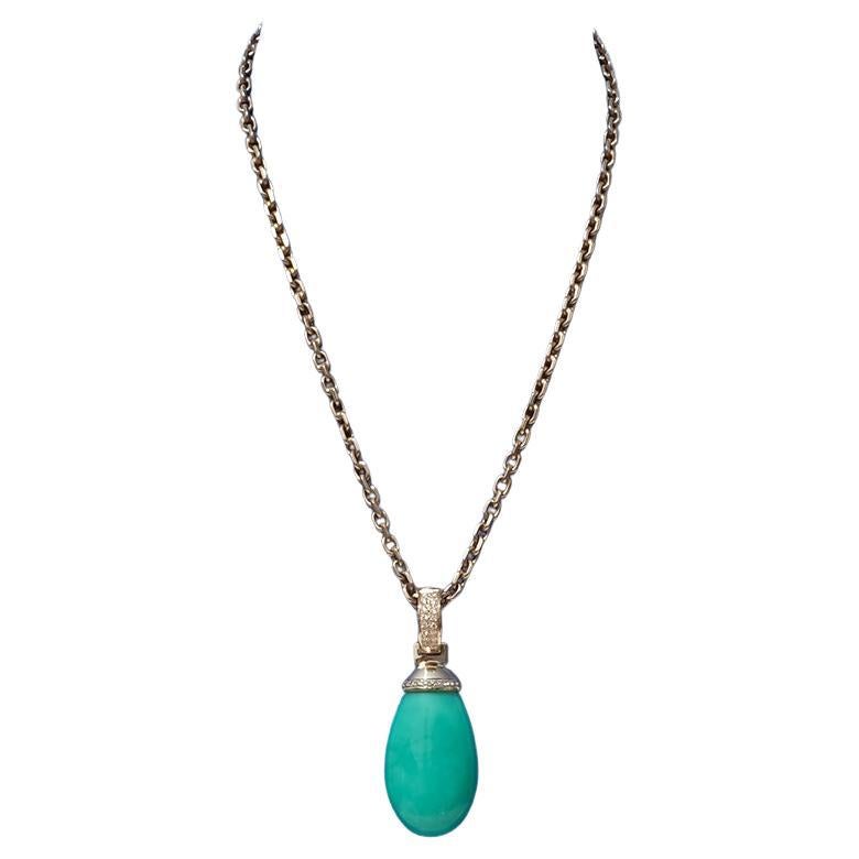 This pendant features a generously sized, drop-shaped chrysoprase in a soft pastel green tone, with an opaque, waxy lustre. The stone is set in 18 karat gold, held by a polished gold cap framed with a row of pavé-set diamonds. The hinged bail is
