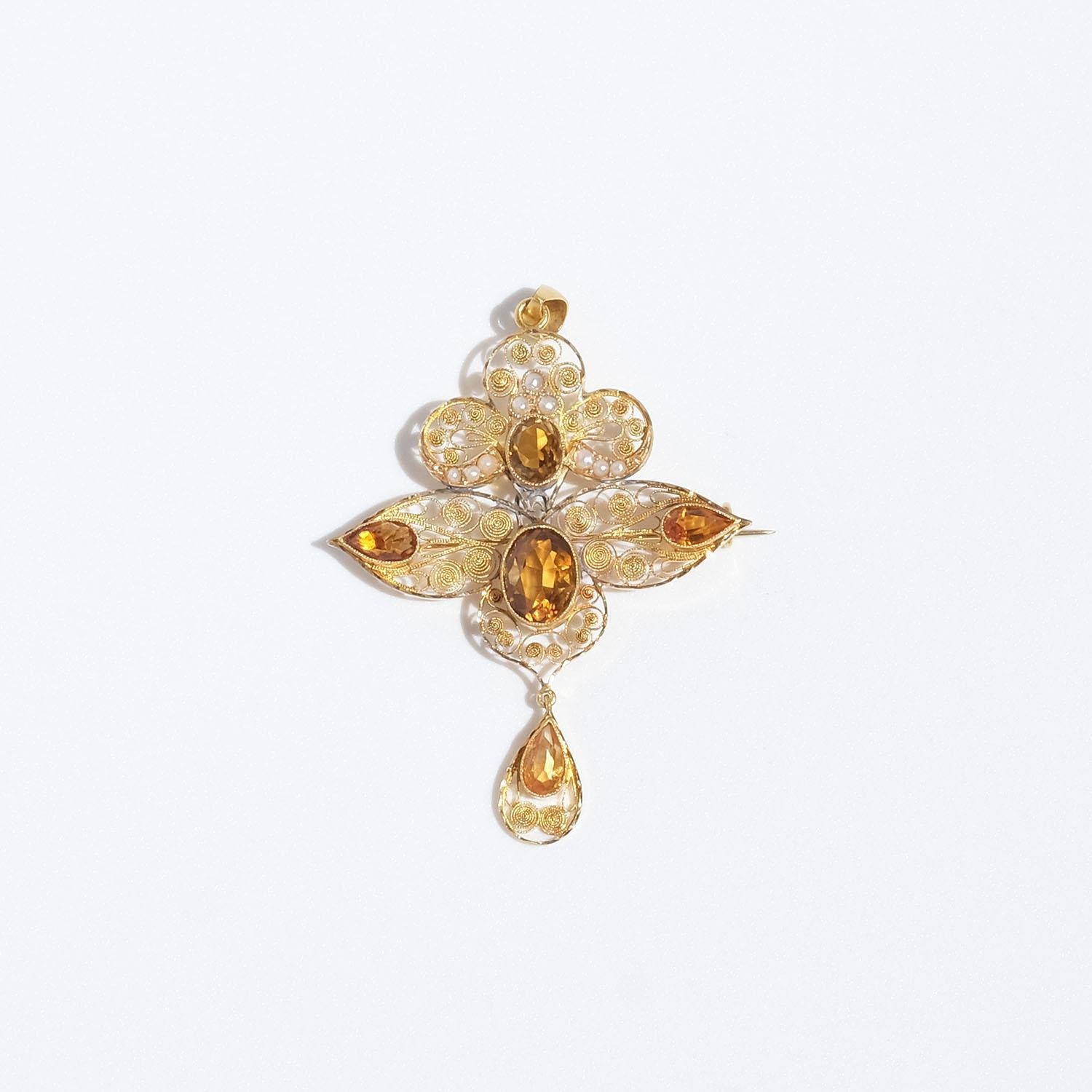 This 18 karat gold brooch is adorned with five flame-coloured, oval and drop-cut faceted, citrines and nine seed beads. The brooch is mainly made of very fine threads that have been soldered together in a beautiful pattern. The brooch is equipped