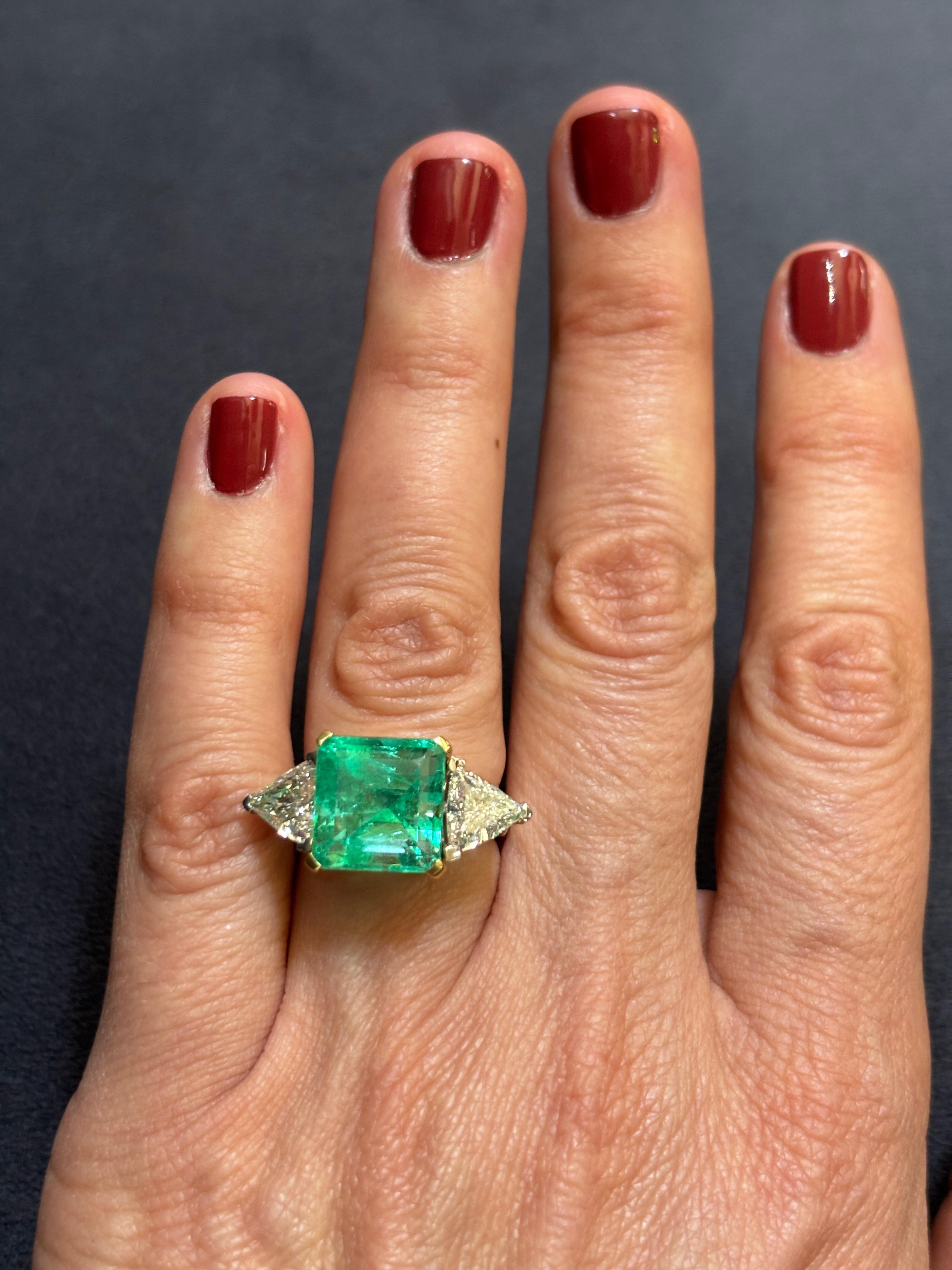 This beautiful 18k gold ring has a central Colombian emerald weighing approximately 8.23 carats. The emerald is flanked by 2 triangular cut diamonds totalling approximately 2.05 carats. It is a truly striking piece.