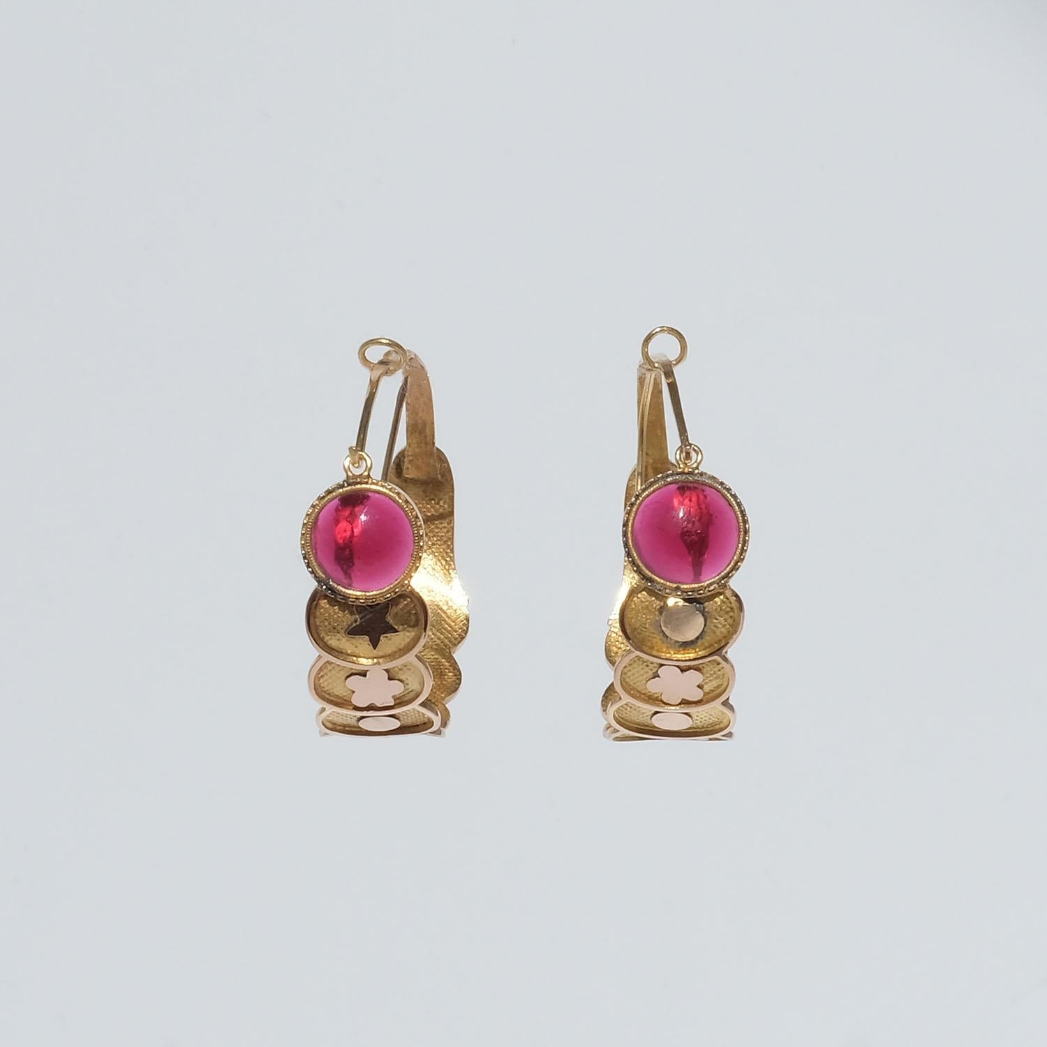These 18 karat gold creole earrings are shaped with overlaping round discs which are decorated with flowers and circles in rose gold. In front they are decorated with a cabochon cut red glass stone. The earrings open and close with a hinged