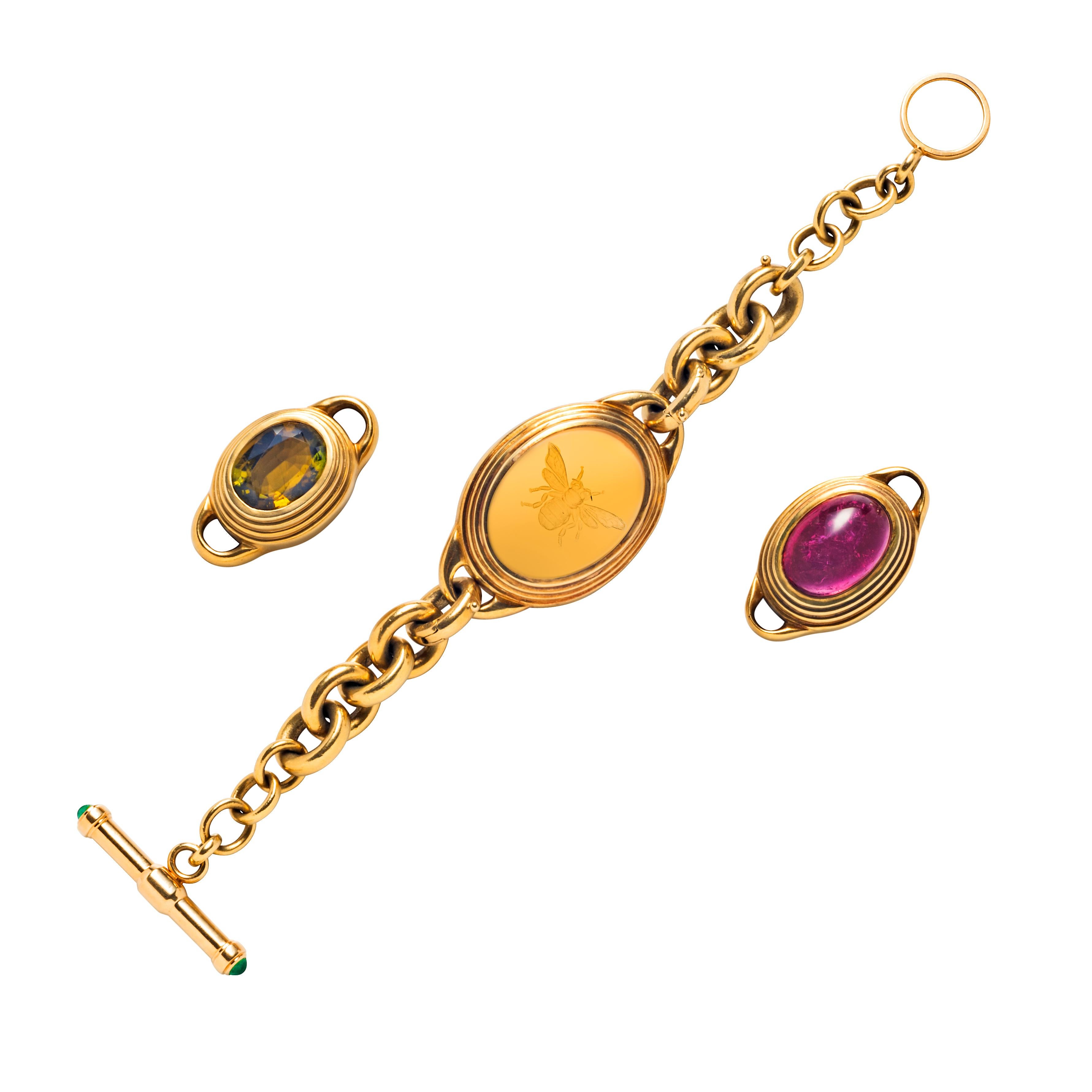 A curb link bracelet with interchangeable center pieces, featuring an oval citrine cabochon intaglio of a bee motif, an oval pink tourmaline cabochon and an oval mixed-cut green tourmaline; the toggle ends set with cabochon emeralds; mounted in 18k