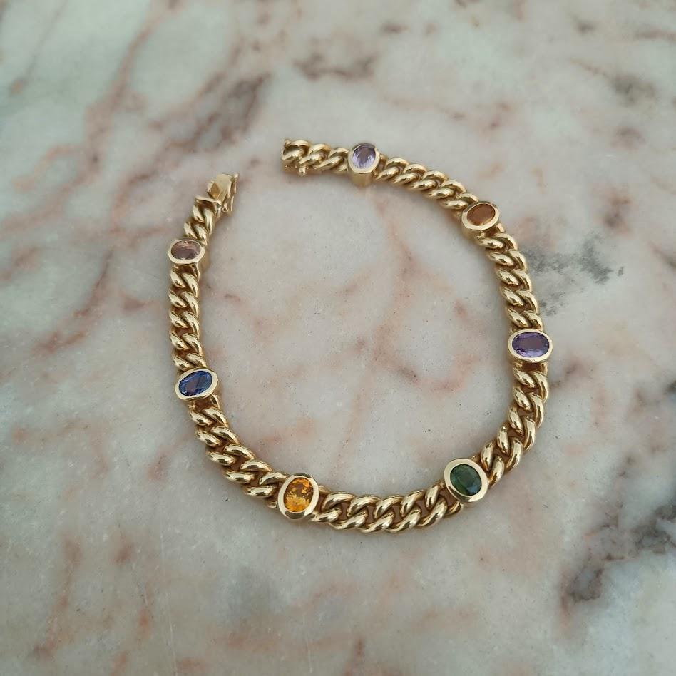 Elegante bracciale realizzato in oro giallo 18 carati, caratterizzato da una classica e sofisticata catena a maglie. Lungo il bracciale sono incastonate sei pietre ovali naturali sfaccettate, ognuna con una tonalità diversa che conferisce al pezzo