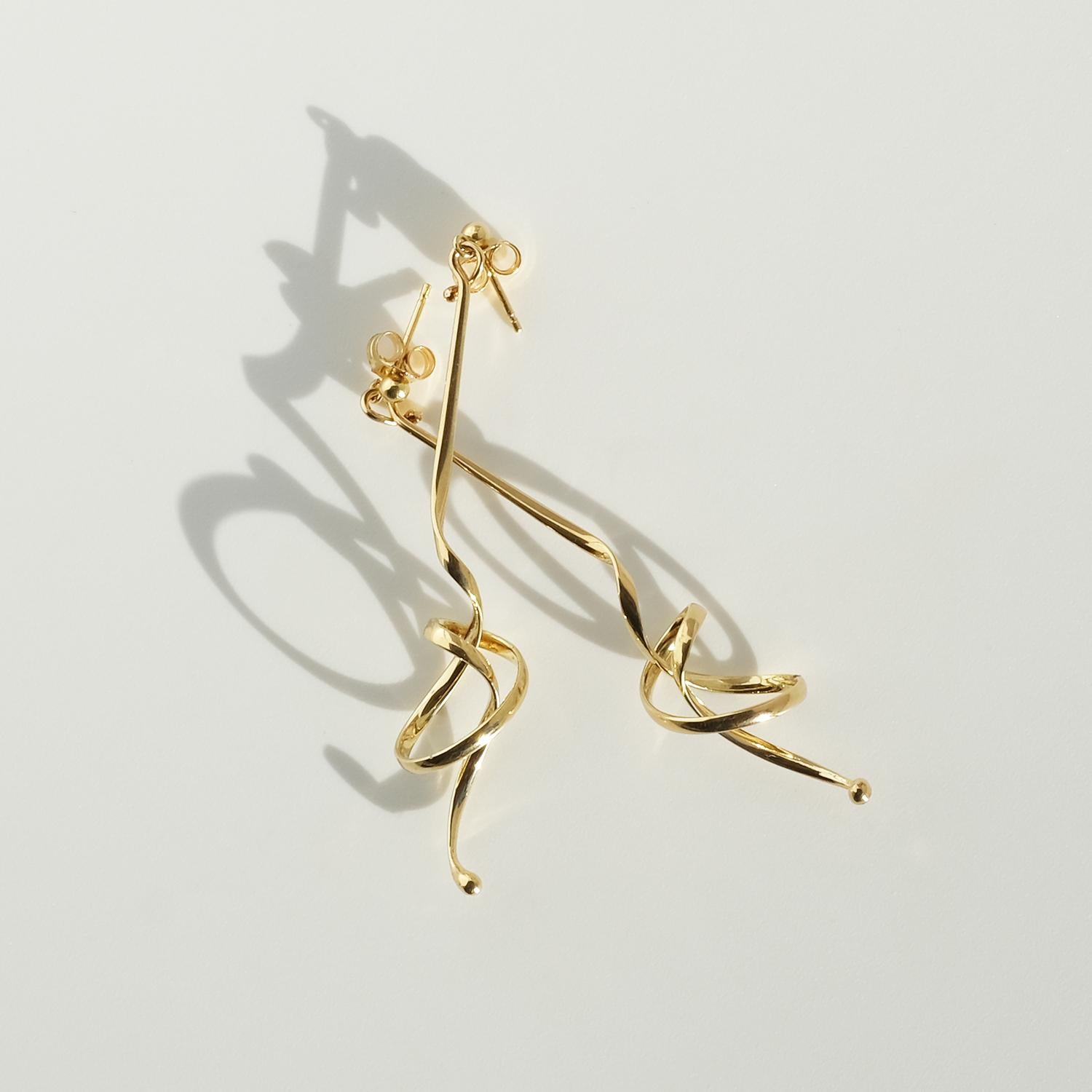 Questi orecchini vintage in oro 18 carati, intitolati Forget Me Knot, presentano forme lunghe e fluide costruite attorno a un motivo scultoreo di nodi. Ogni orecchino inizia con un semplice perno e si estende in una goccia sottile e tortuosa che si