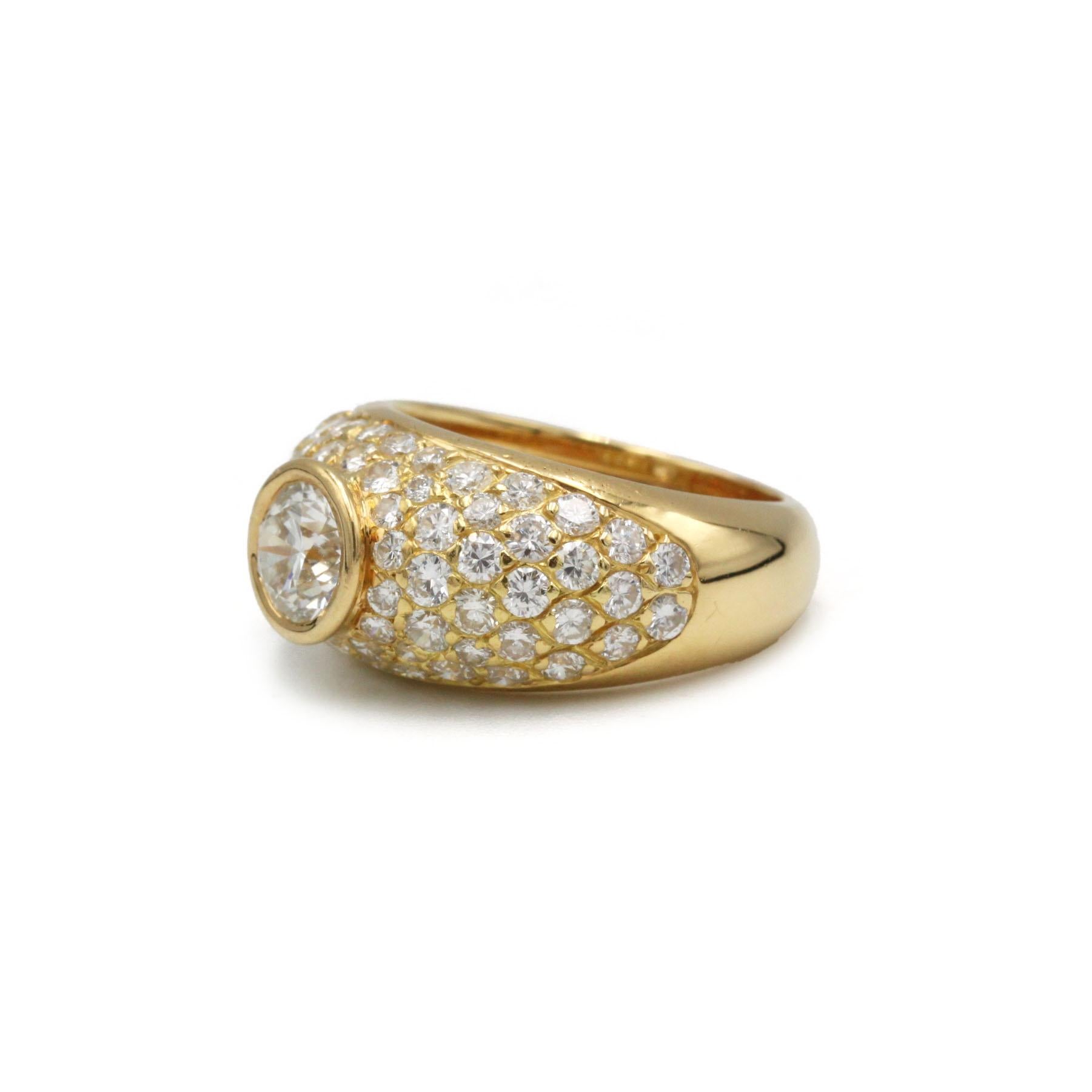 Este impresionante anillo de oro amarillo de 18 quilates presenta un diseño atrevido y escultural totalmente engastado con pavé de diamantes talla brillante, centrado por un prominente diamante redondo de aproximadamente 1,00 quilate, enmarcado por