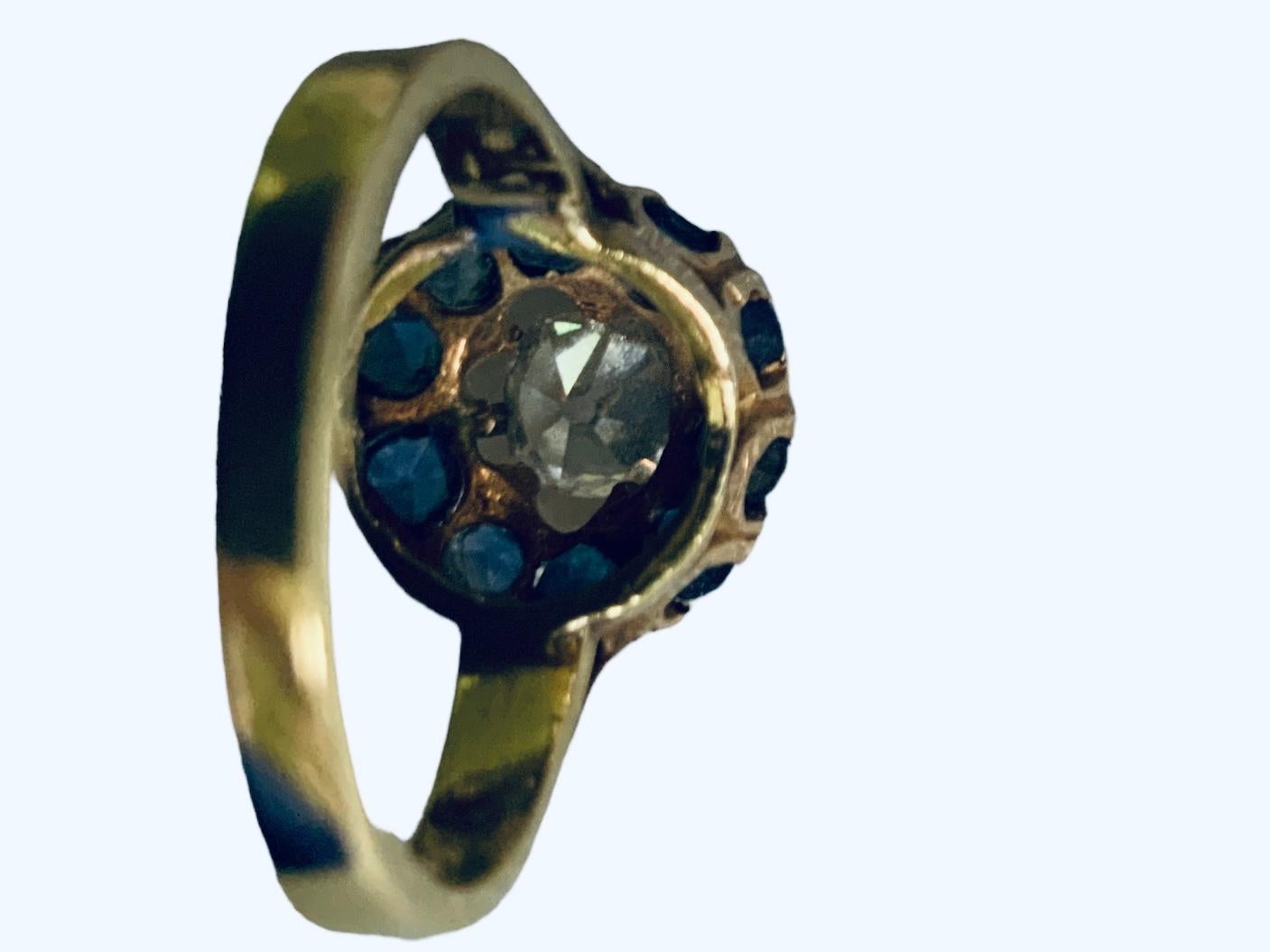 Questo è un anello con diamanti e iolite in oro 18 carati. Raffigura un anello a grappolo in oro giallo che contiene un diamante a forma di vecchia miniera del peso di circa 0,74 carati, di colore H-I e di purezza VS-1. La spalla intorno al diamante