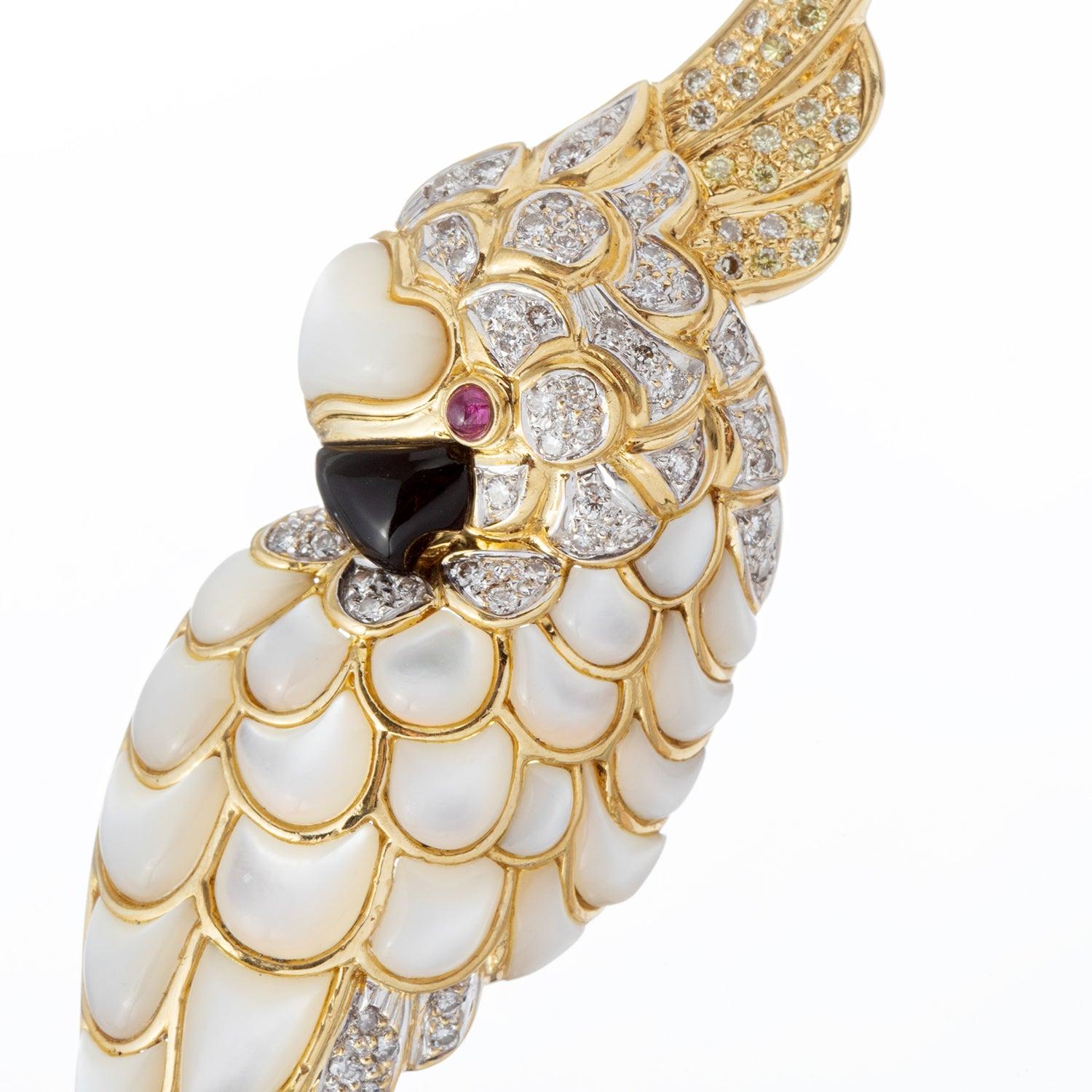 Cockatoo pendant brooch in 18k yellow gold, featuring round-cut diamond-set head and tail feathers, as well as carved mother-of-pearl feathers and a single ruby eye.

Double pin stem backing.  Loop at top of back so it can also be worn on a neck