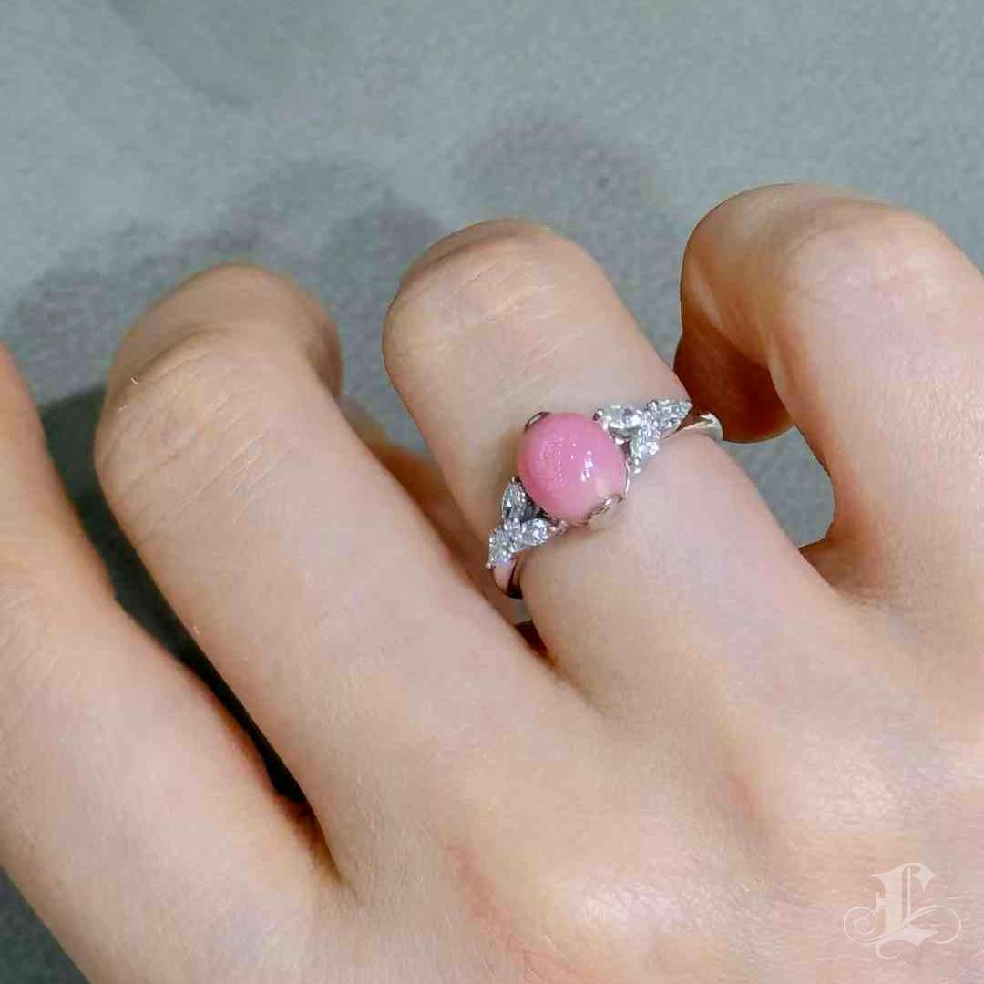 A timeless expression of feminine grace, this dainty three-stone ring features a perfectly round conch pearl of 2.80 carats in a captivating flamingo pink hue. The pearl is delicately framed by 0.40 carats of brilliant diamonds, arranged like