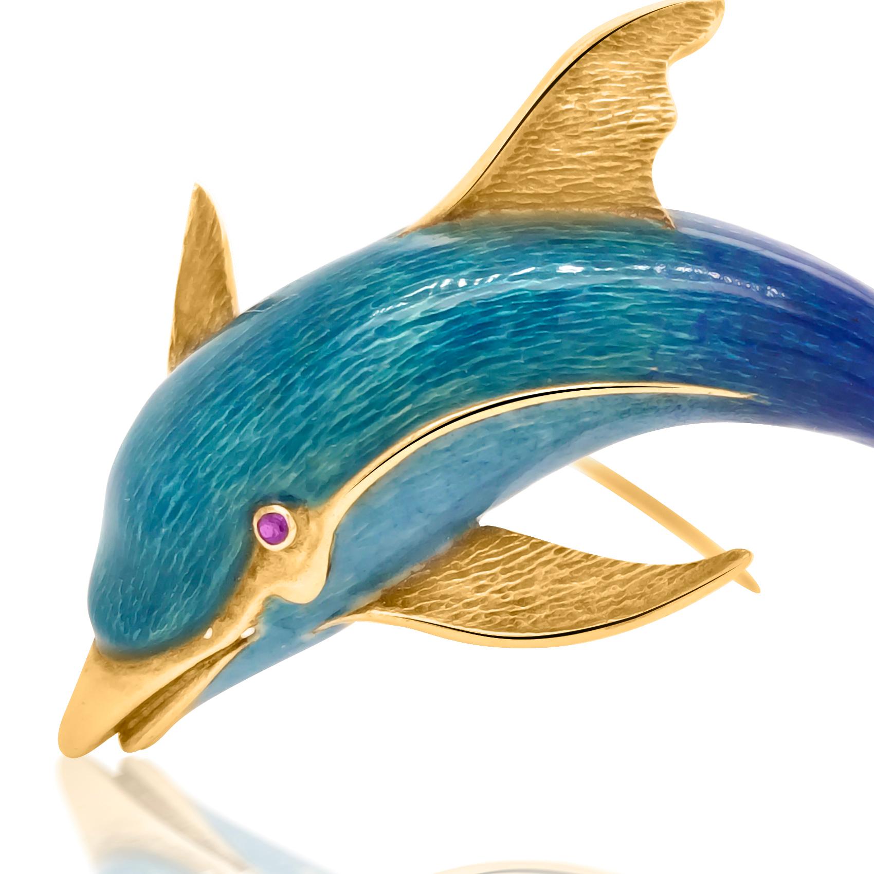 This adorable dolphin pin brooch is crafted in solid 18-karat yellow gold, weighing 16.68 grams and measuring 63mm long x 41mm wide. The eye is an approx. 0.02-carat ruby. Highlighting its body ornately with blue and ultramarine blue enamel and gold