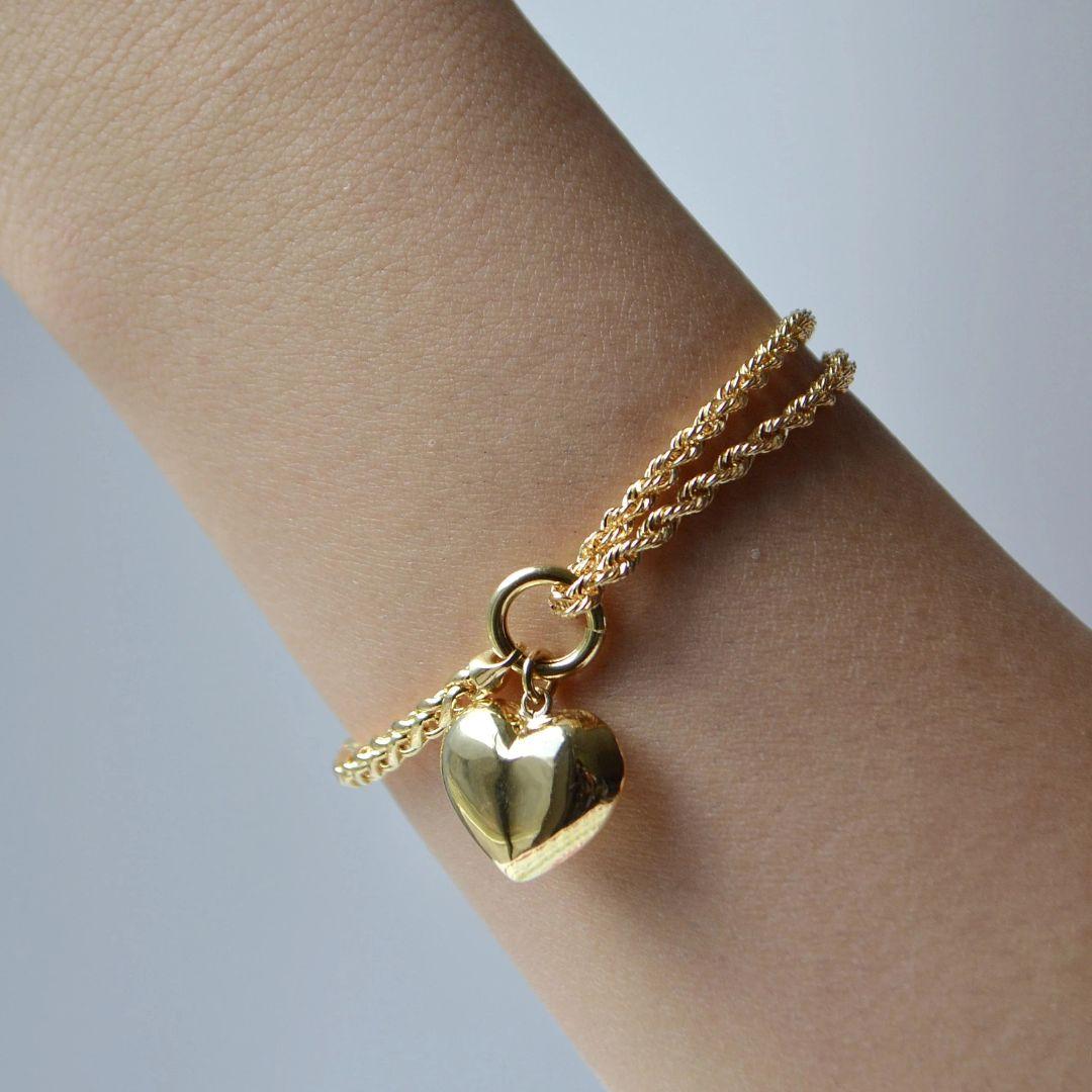 Realizzato in oro giallo 18 carati, questo squisito braccialetto presenta un intricato design a catena con corda e treccia, elegantemente ornato da un delicato charm a forma di cuore. La combinazione di texture aggiunge profondità e dimensione,