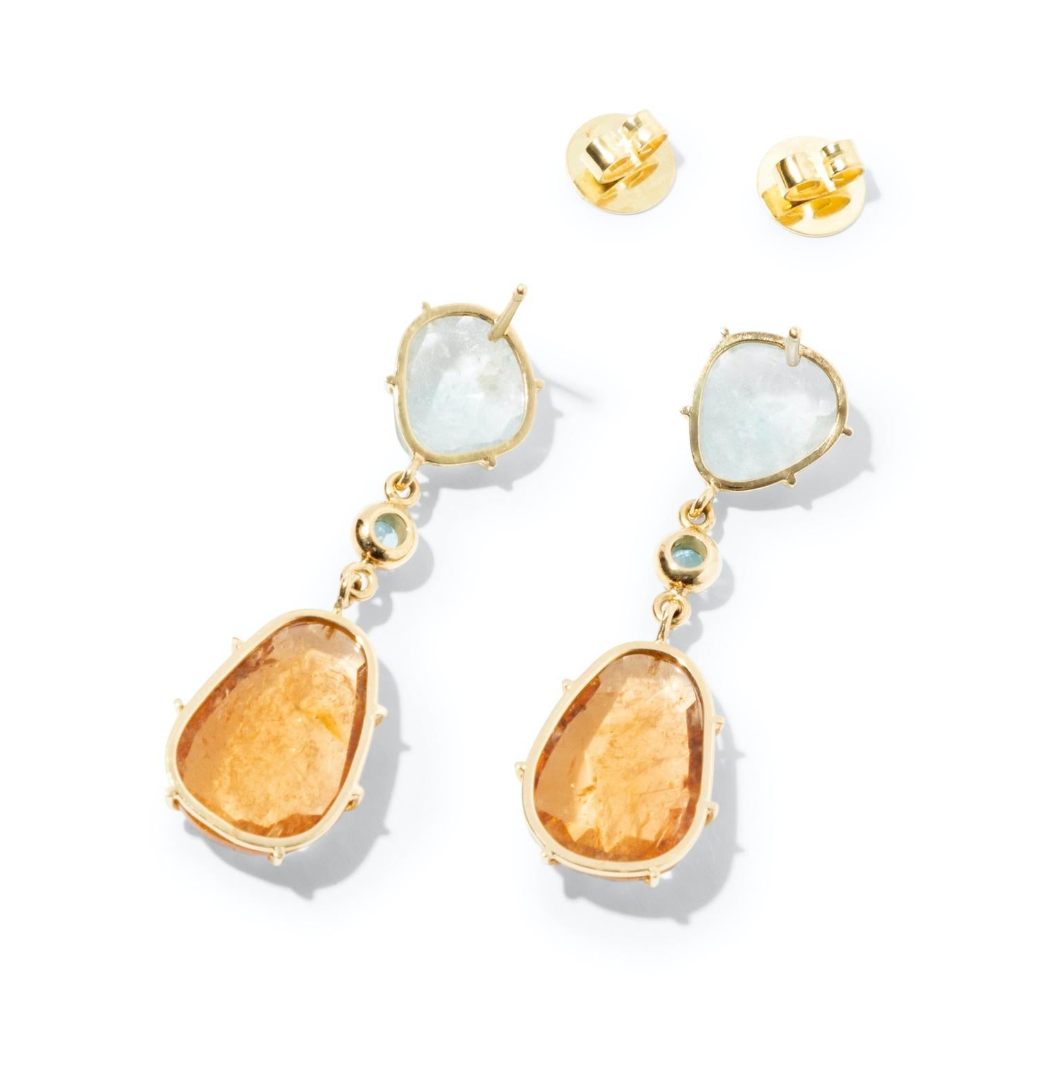 18k gold tourmaline drop earrings in an unusual shade of saturated orange and sky blue. 
These vibrant colors combined with the random cut of the gemstones will lend a boho chic vibe to your wardrobe. Two sparkling blue brilliant cut topaz gemstones
