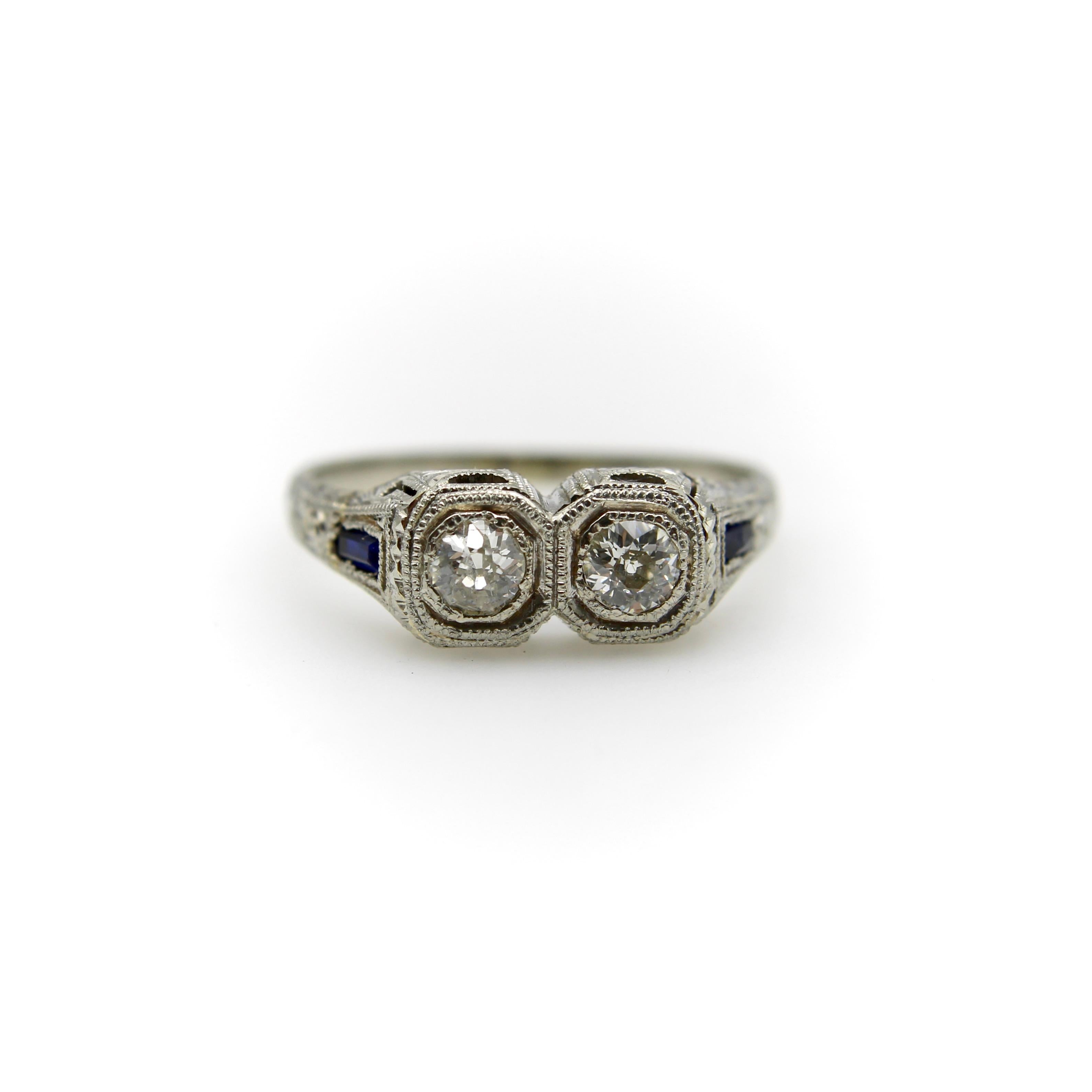 Este impresionante anillo de oro blanco de 18 quilates, diamantes y zafiros pertenece a la cúspide de las épocas eduardiana tardía y art déco temprana, hacia 1915-1920. Está engastado con dos diamantes talla Old Mine colocados uno al lado del otro