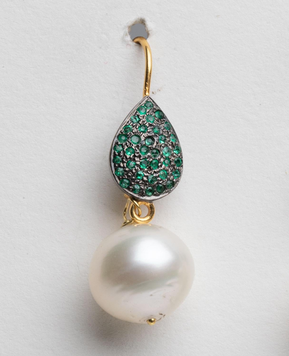 A fresh water pearl drop earring dangling from a pear-shaped French back earring wire with round, faceted emeralds in a pave` setting.  18K gold, for pierced ears.  By Deborah Lockhart Phillips