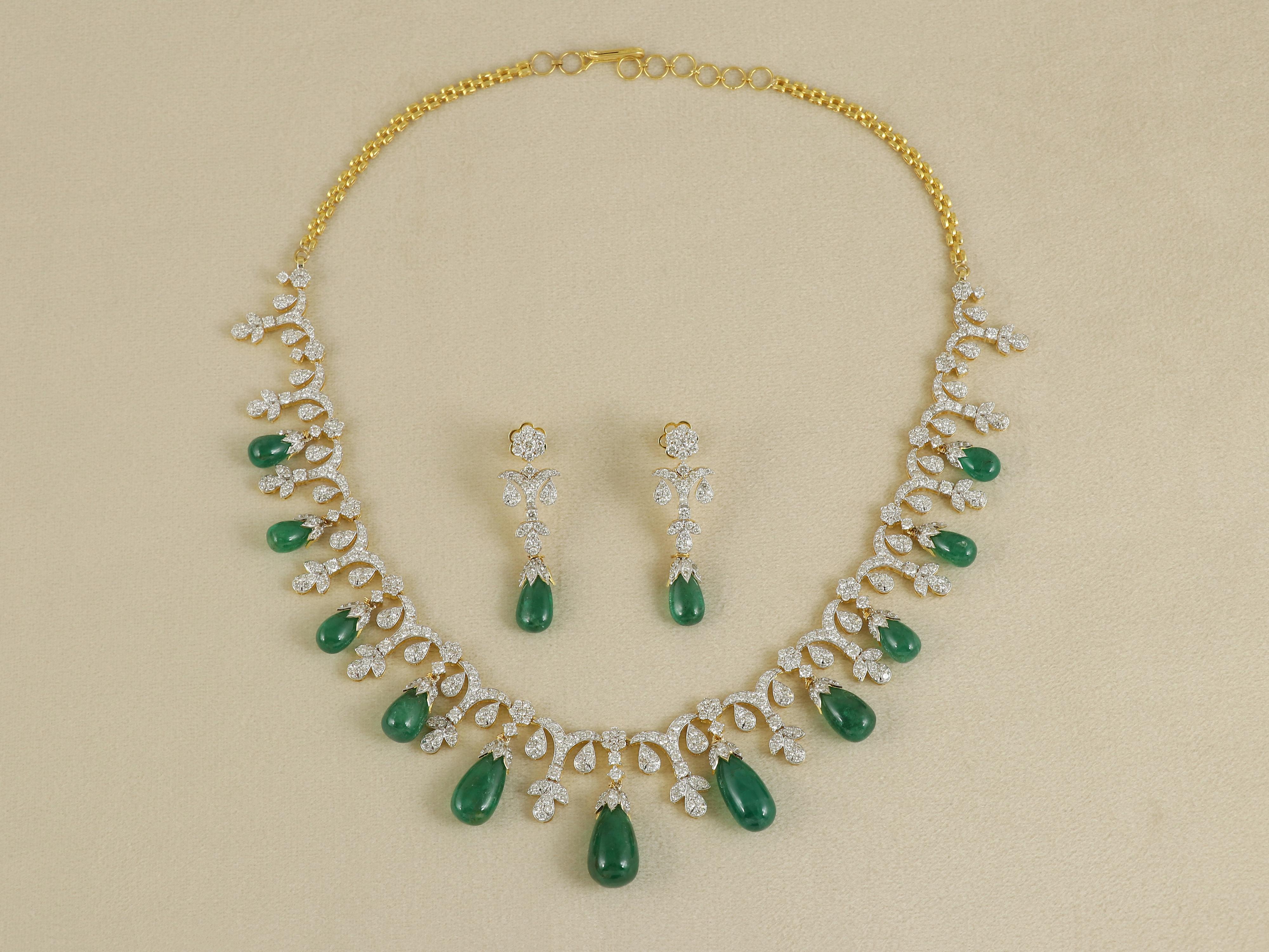 Una miscela senza tempo di eleganza e lusso, questa squisita collana è caratterizzata da gocce di smeraldo graziosamente sospese da cappucci incastonati di diamanti. Gli smeraldi incastonati sono naturali e provengono dalle venerate miniere di